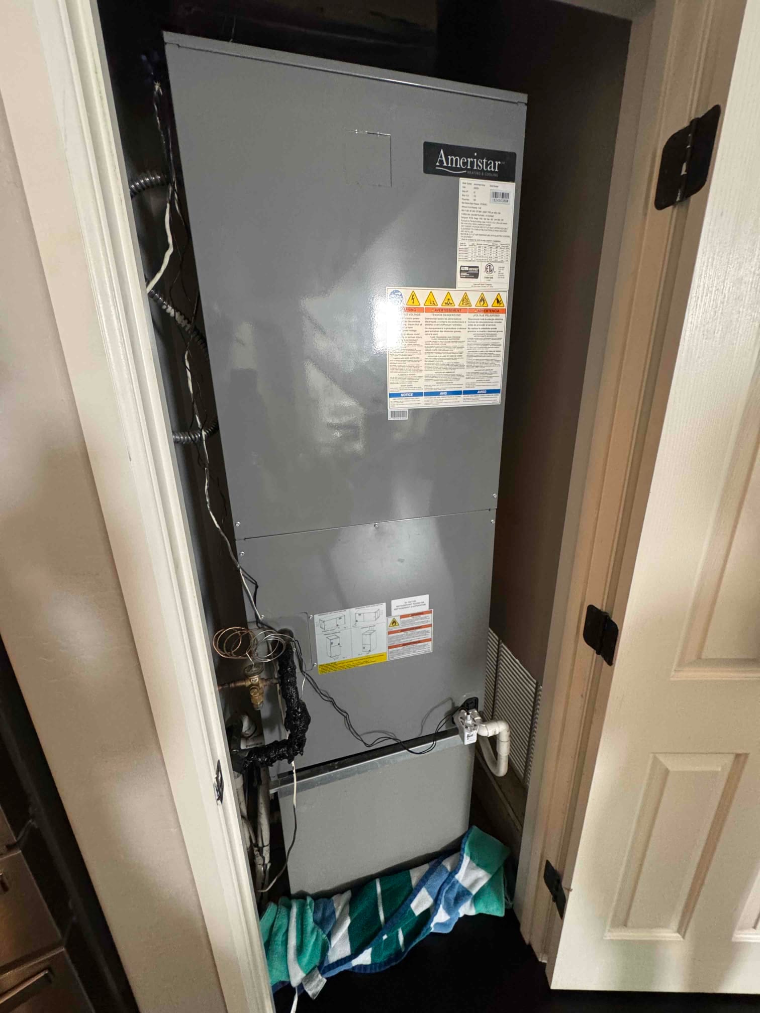 Indoor air handler in a closet with condensate drain line, cleanout, and trap visible; towels placed below for leak control.