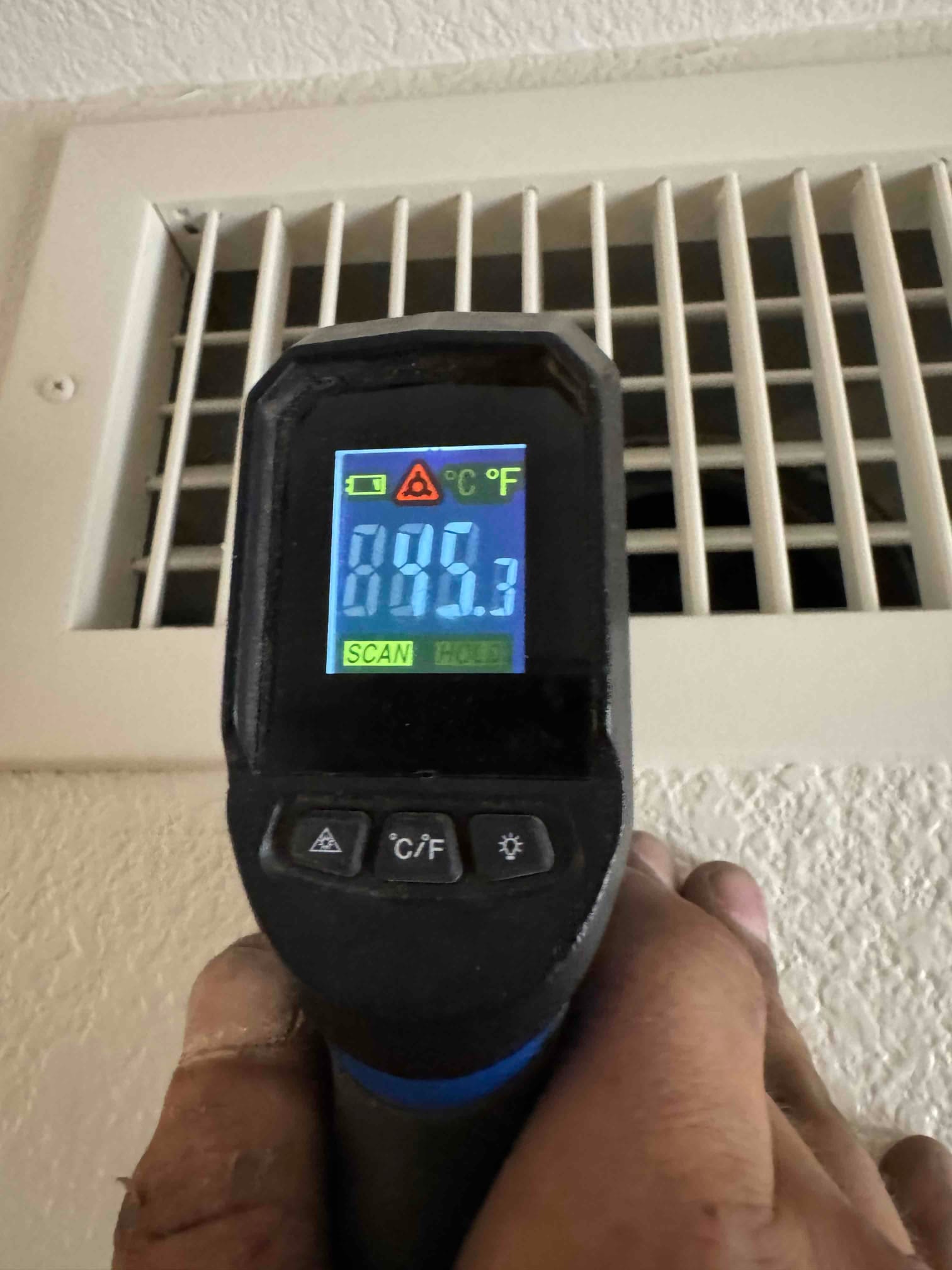 Infrared thermometer measures air temperature at a wall grille, displaying 85.3 degrees Fahrenheit during commissioning checks.