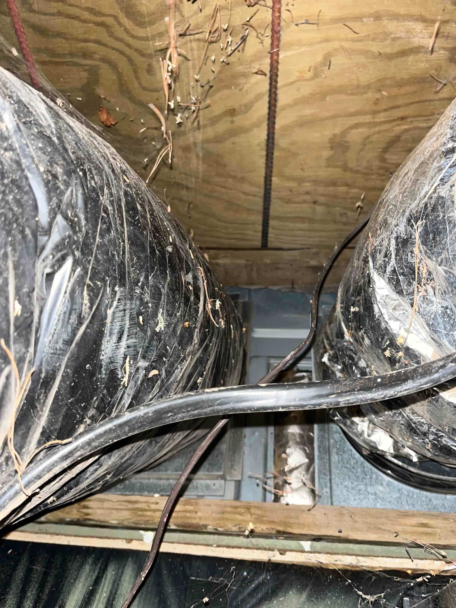 Two insulated flexible ducts route into a metal air handler plenum in an attic, with wiring and debris visible.