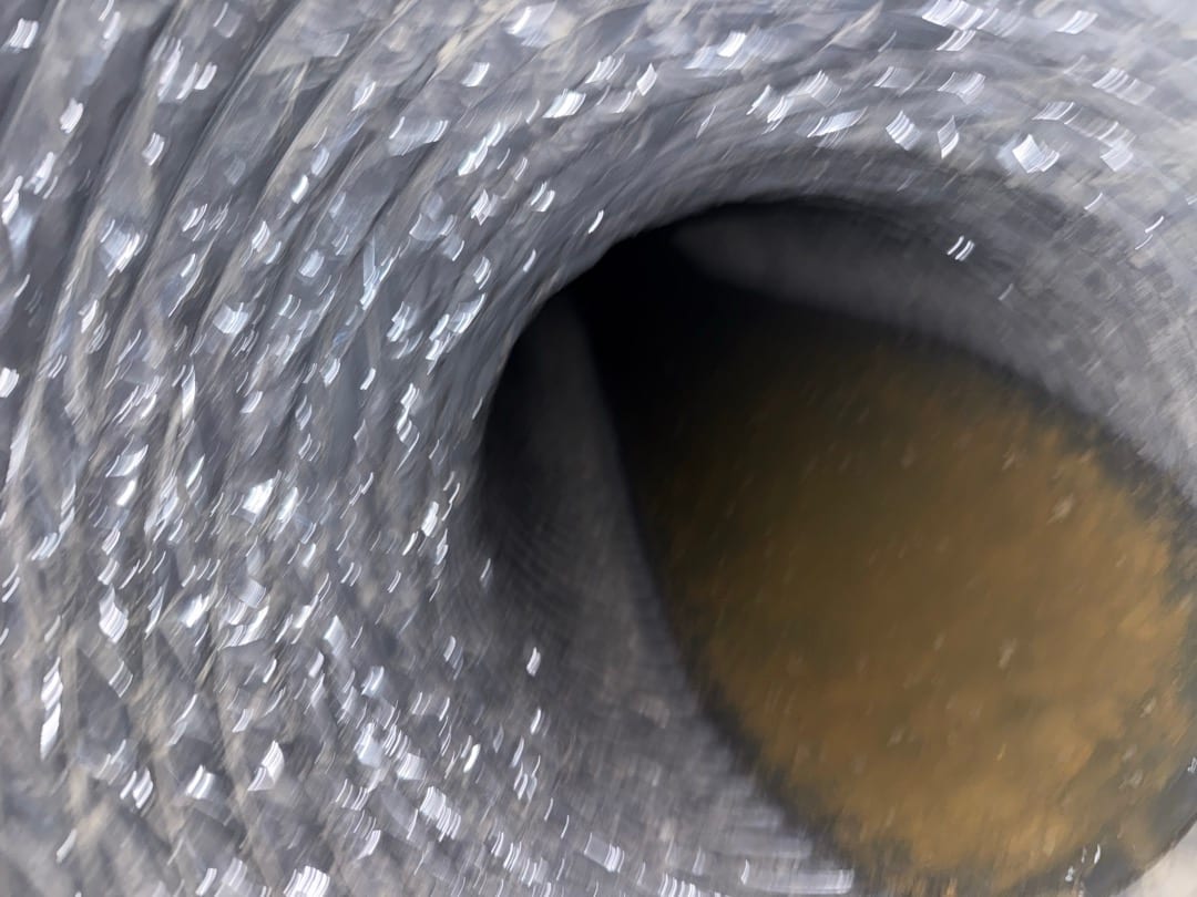 Interior view of flexible HVAC duct showing corrugated lining and accumulated dust or debris on the bottom surface.