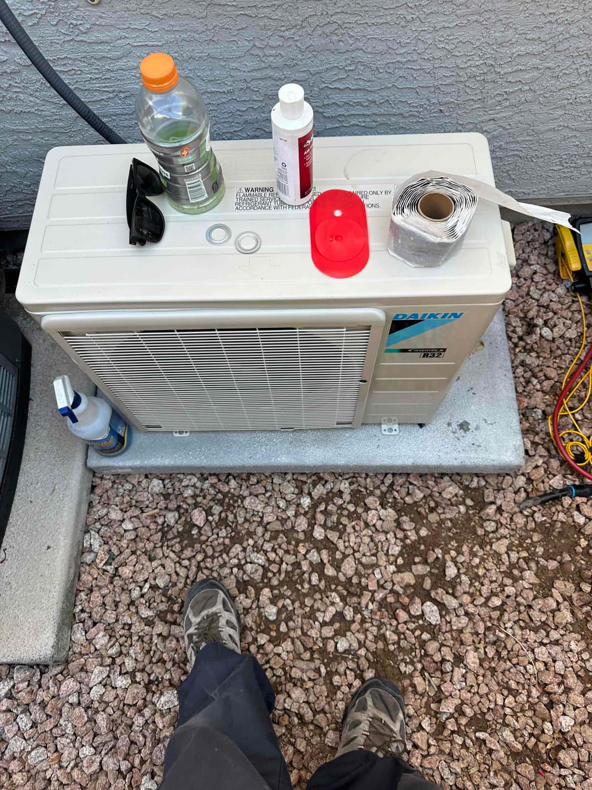 Mini-split outdoor unit set on a level pad with tools and materials on top during installation.