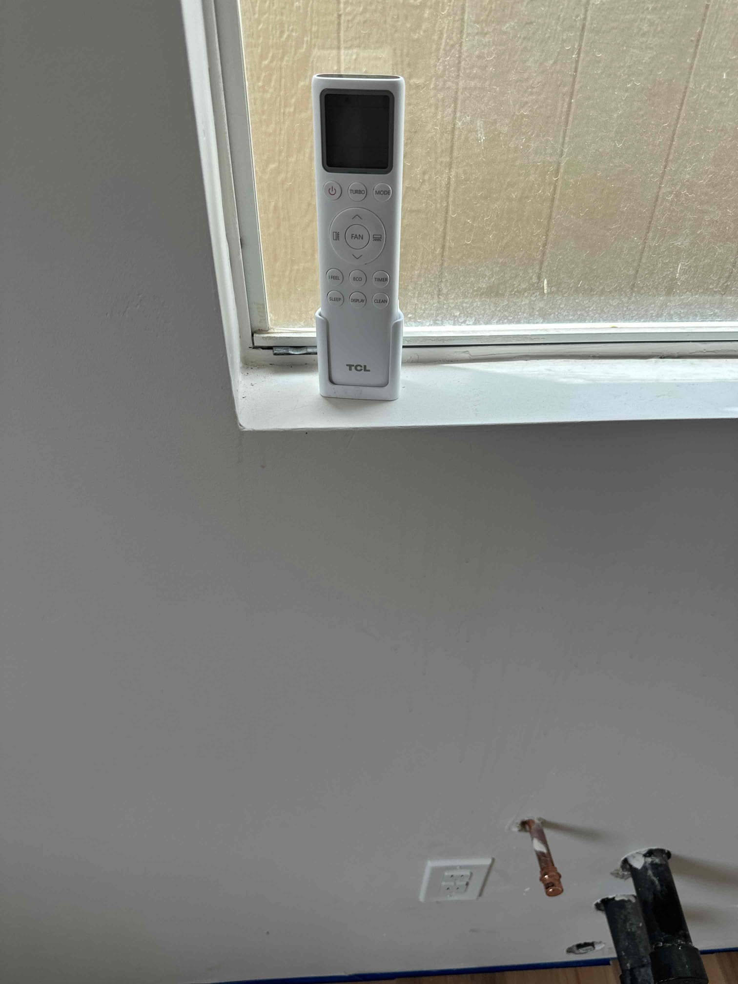 Mini‑split remote in a cradle on the windowsill above the indoor install location with stubbed refrigerant line and wall penetration.