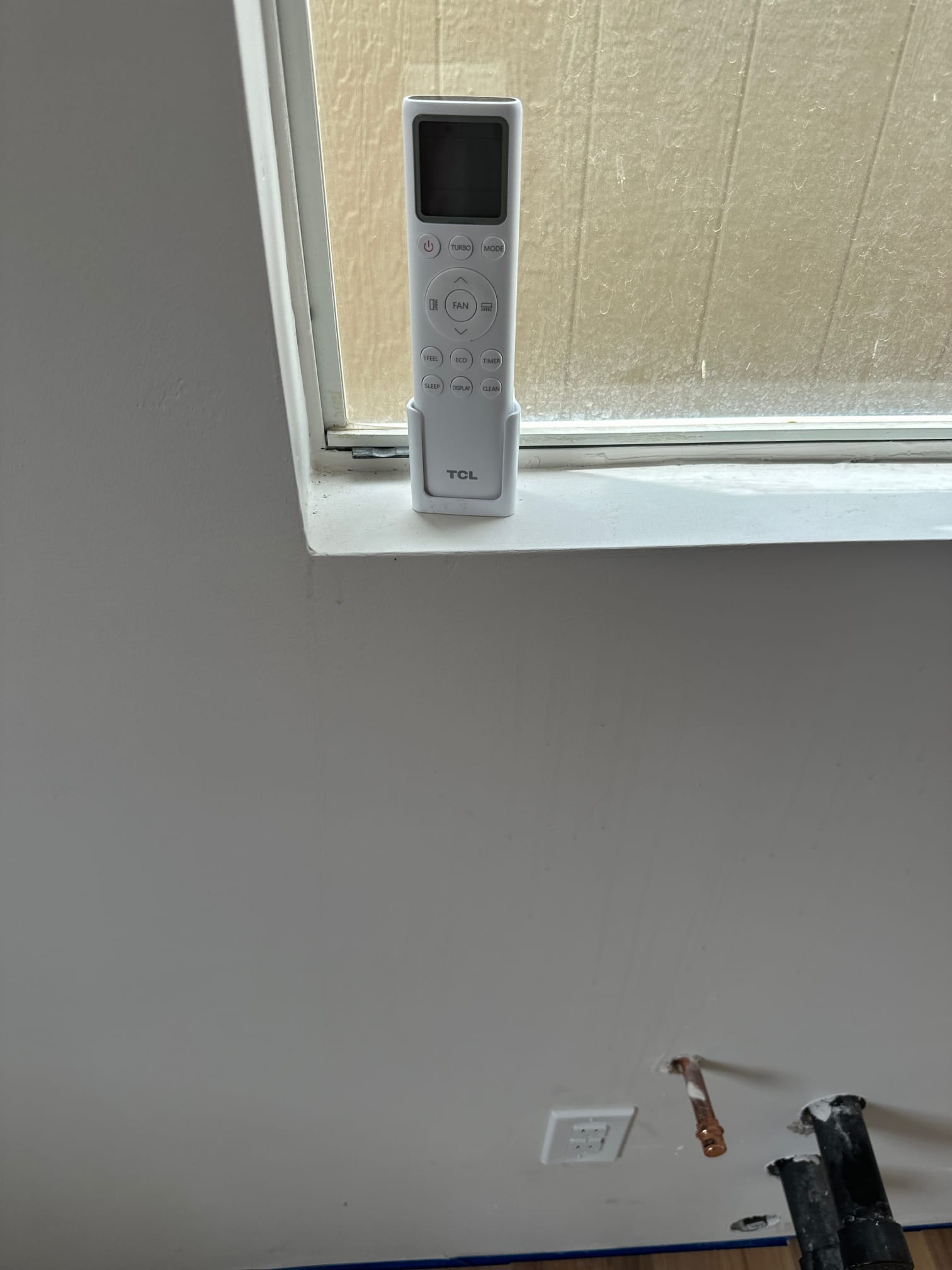 Mini-split remote on a window sill above the indoor install location with wall penetration and copper line stubbed through.