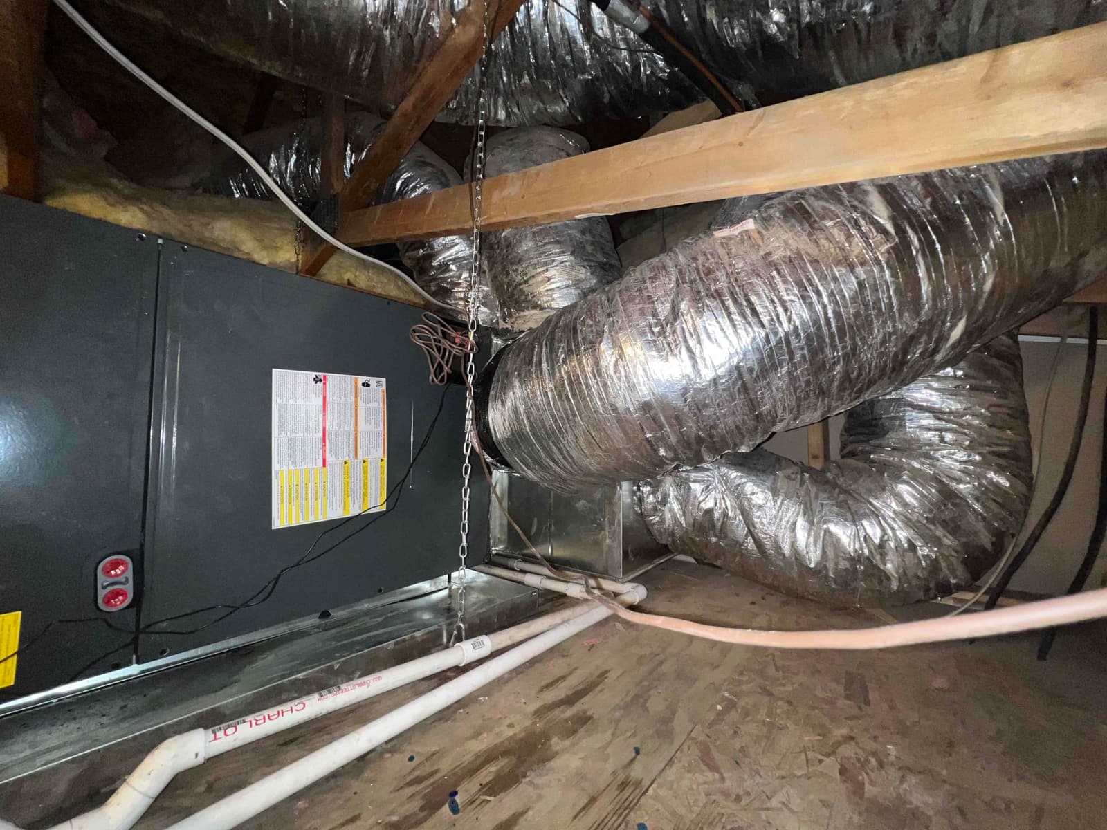 New air handler installed in attic with connected flexible ductwork, secondary drain pan, PVC condensate drain, and hanging support chains.