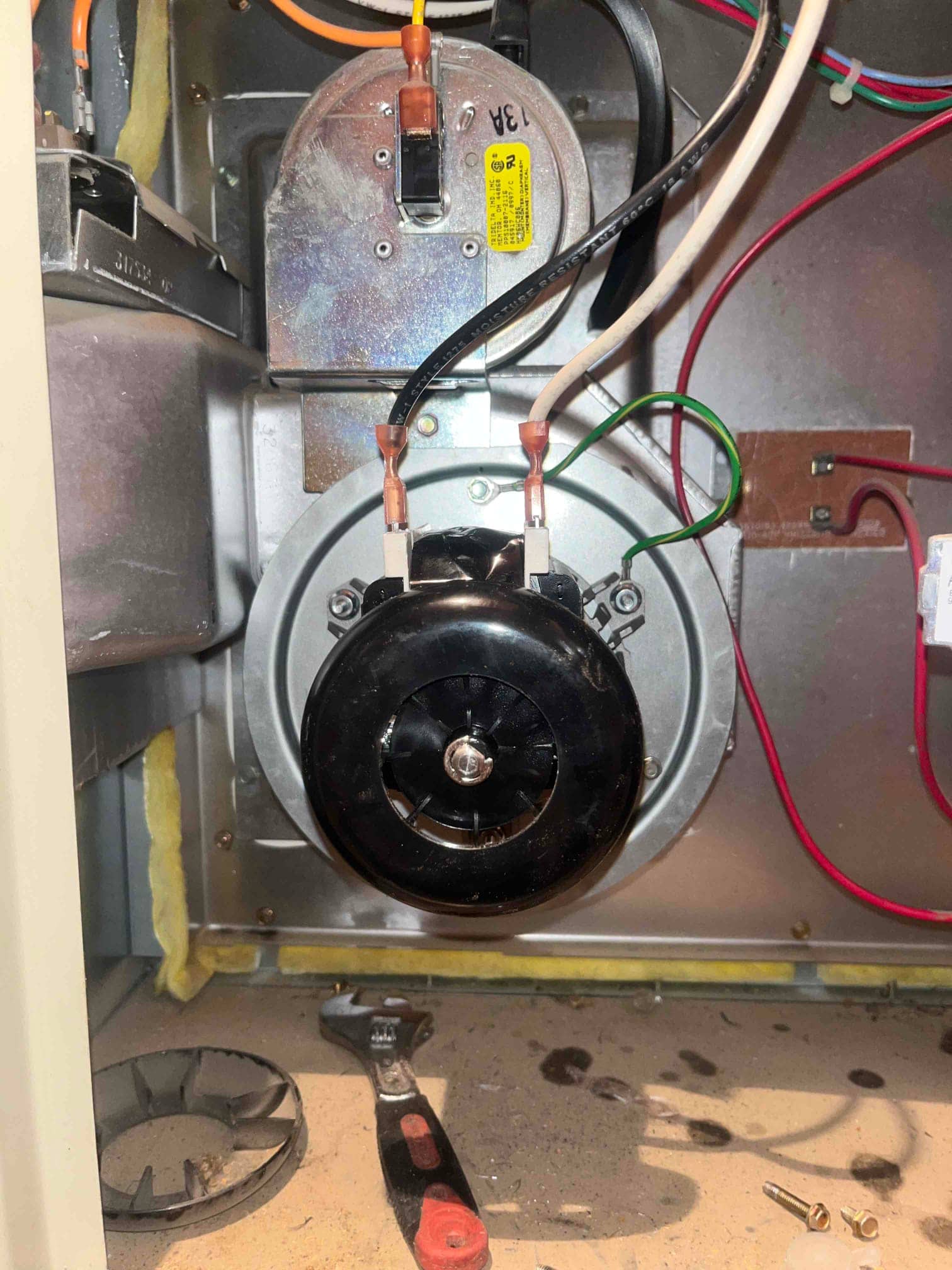 New furnace inducer draft motor installed with connected wiring and mounting hardware, shown inside the furnace cabinet during repair.