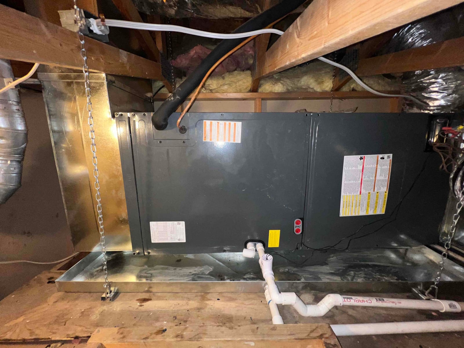 New horizontal air handler suspended over a drain pan with insulated refrigerant lines and PVC condensate drain piped to discharge.