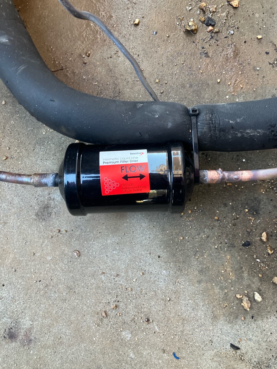 New liquid-line filter drier brazed into the copper line set, with insulation and flow direction indicated on the label.