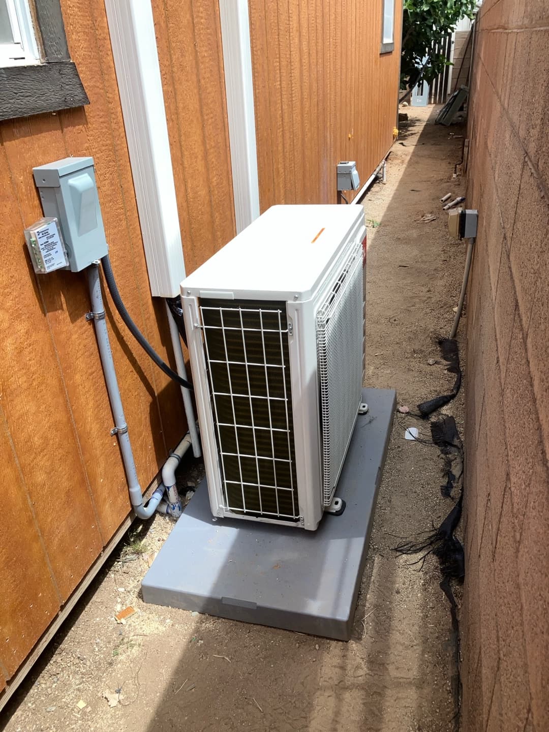 New mini-split outdoor unit set on a level pad with line hide, condensate drain, and weatherproof disconnect installed.