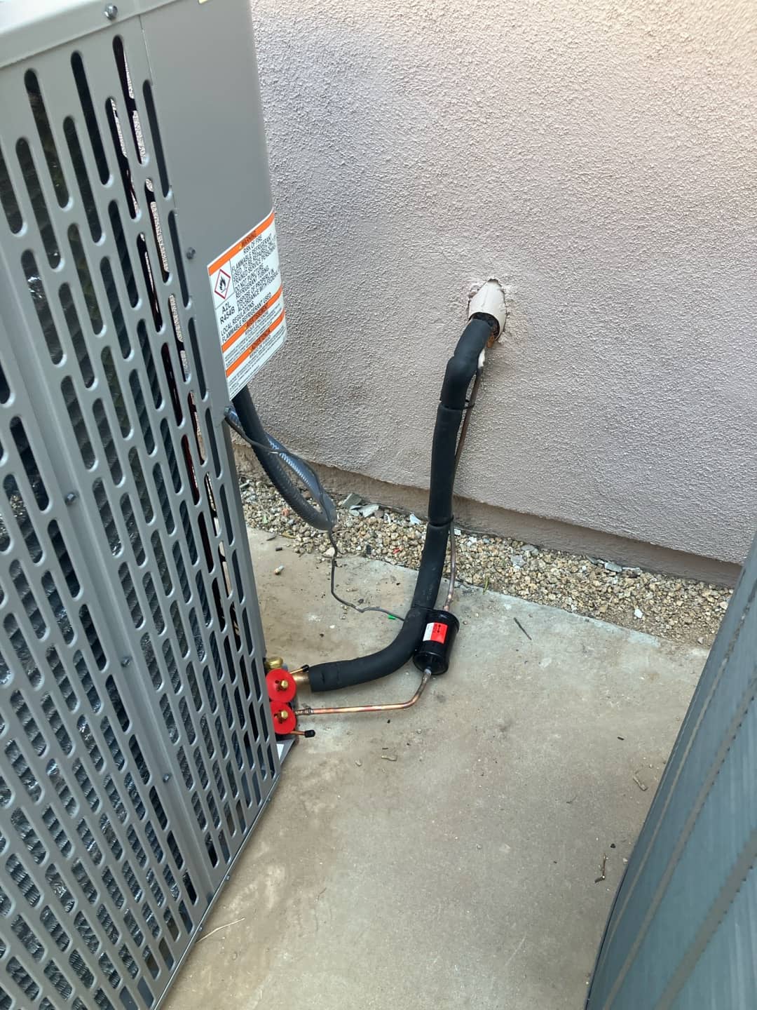 New outdoor condenser with insulated line set, sealed wall penetration, and a liquid-line filter drier installed at the service valves.