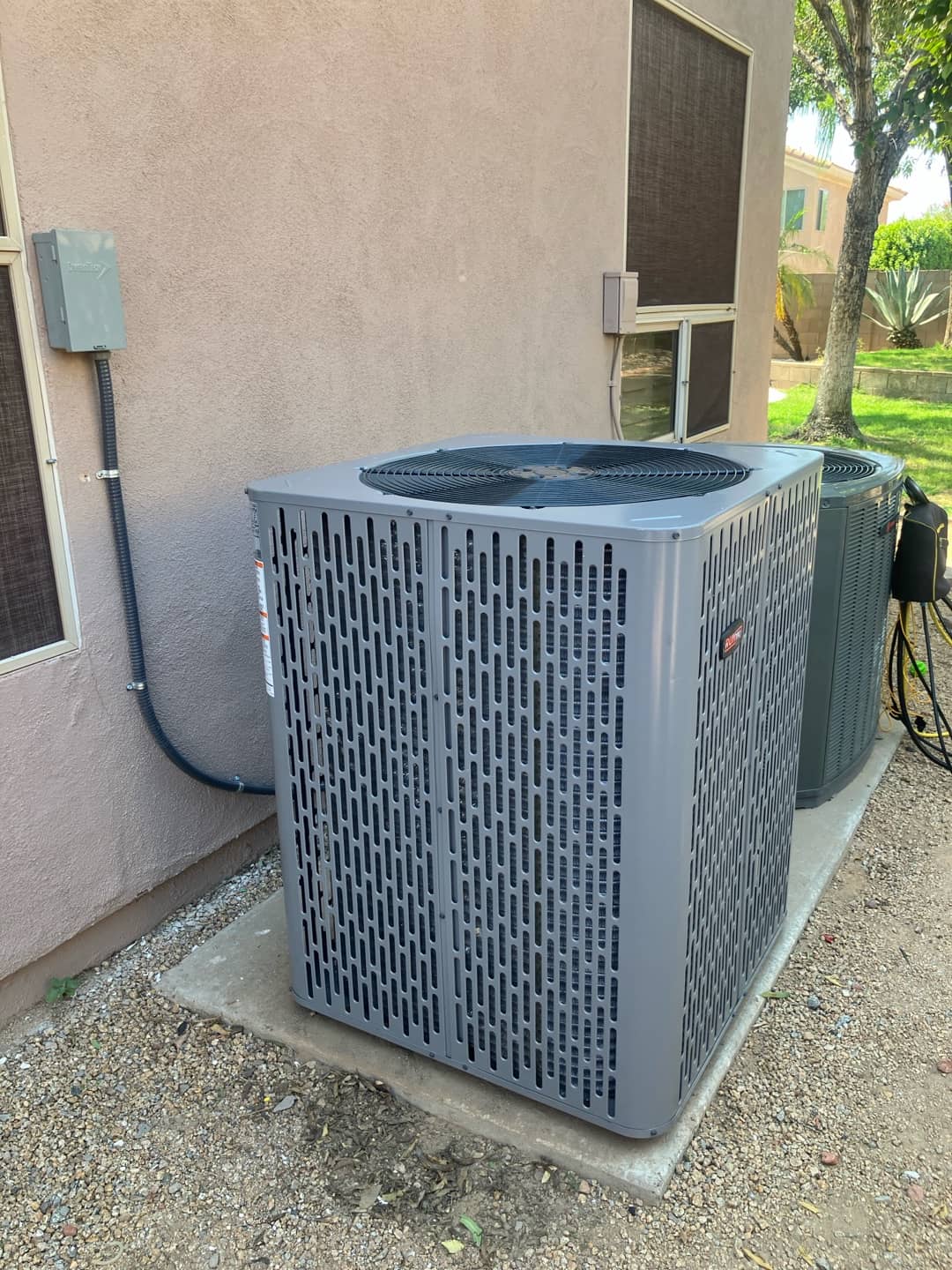 New outdoor condenser set on a level pad with electrical disconnect and conduit installed along the exterior wall.