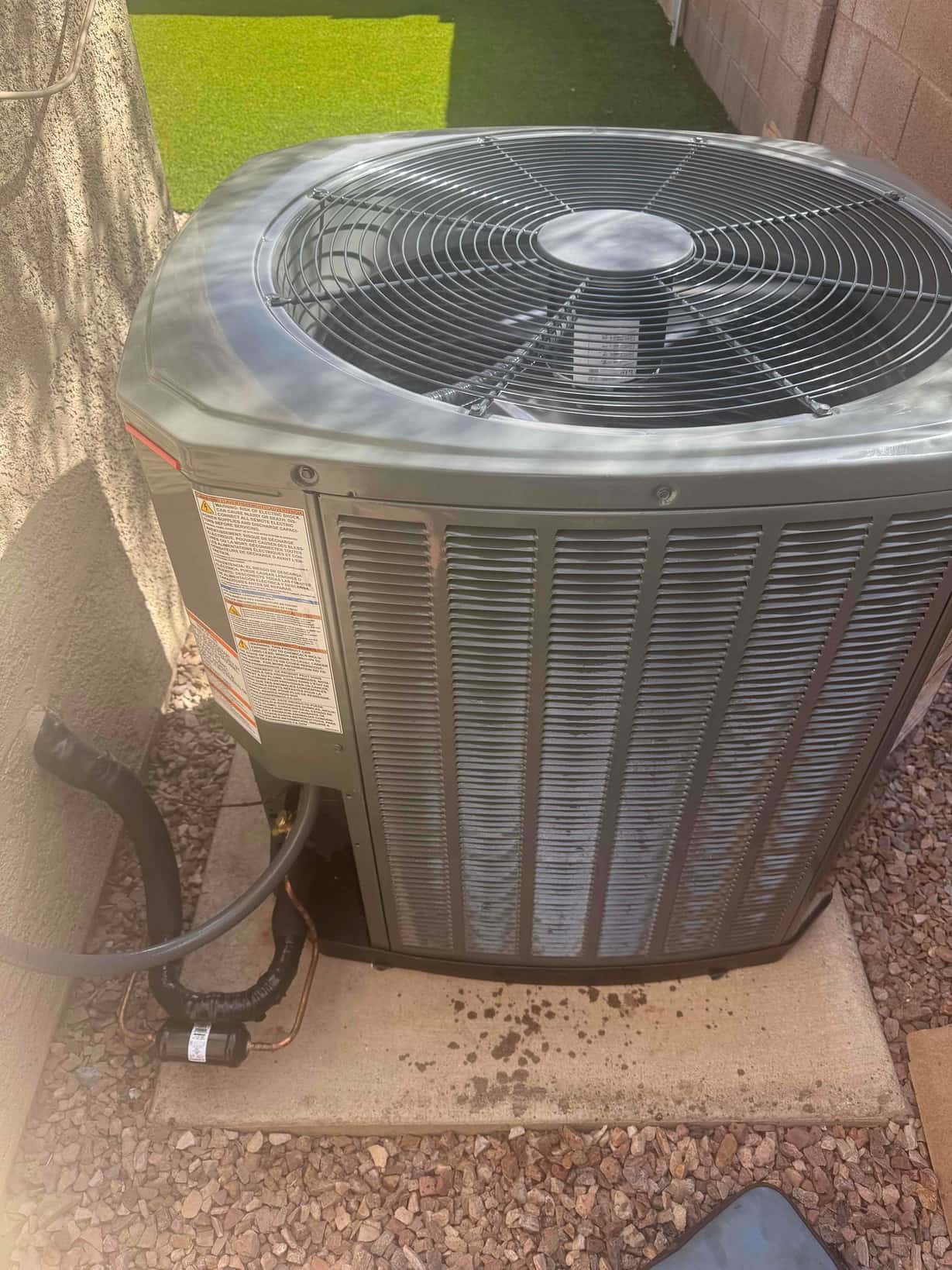 New outdoor condenser set on a level pad with insulated refrigerant lines and sealed wall penetration in a finished yard.