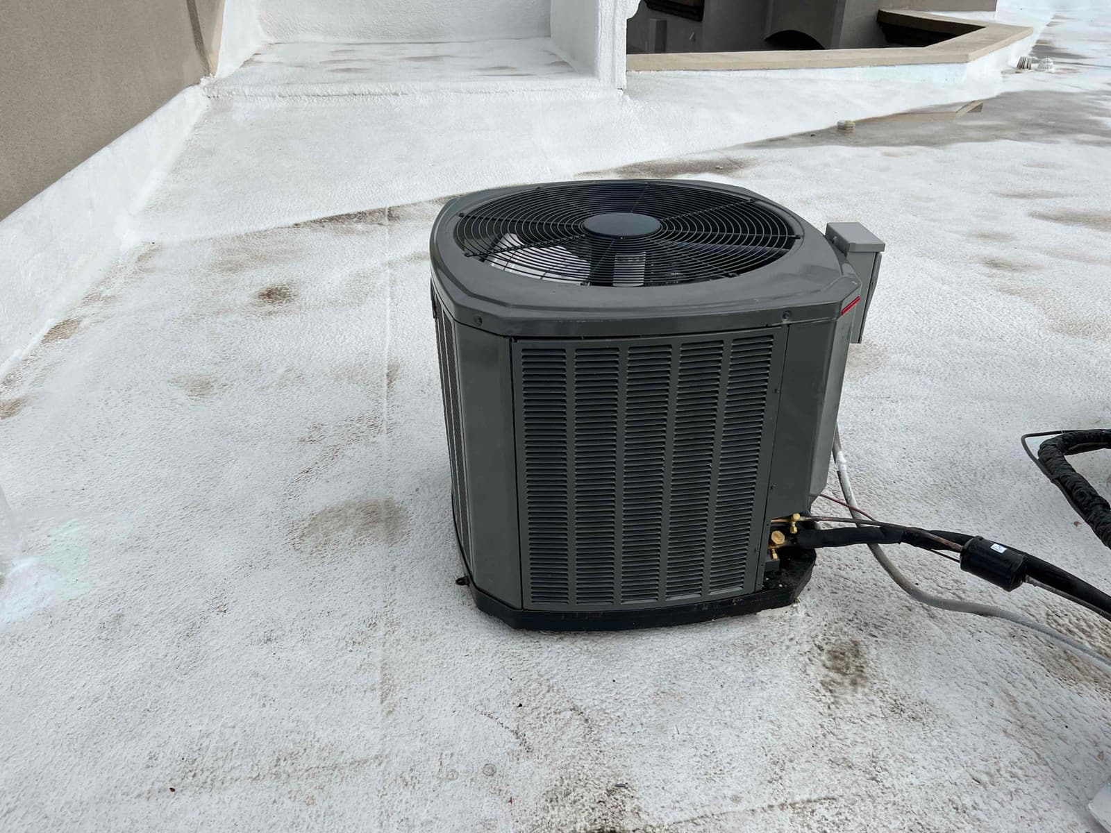 New outdoor condenser set on a level pad with insulated refrigerant lines and electrical whip routed to the unit.