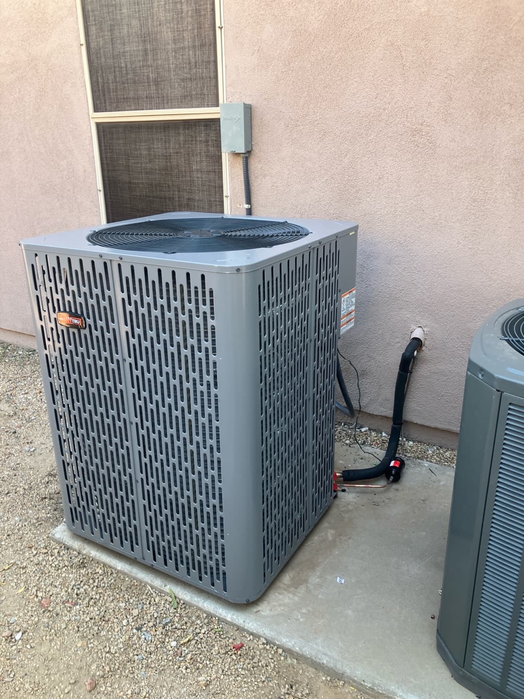 New outdoor condenser set on a level pad with insulated refrigerant lines and weatherproof disconnect mounted on the wall.