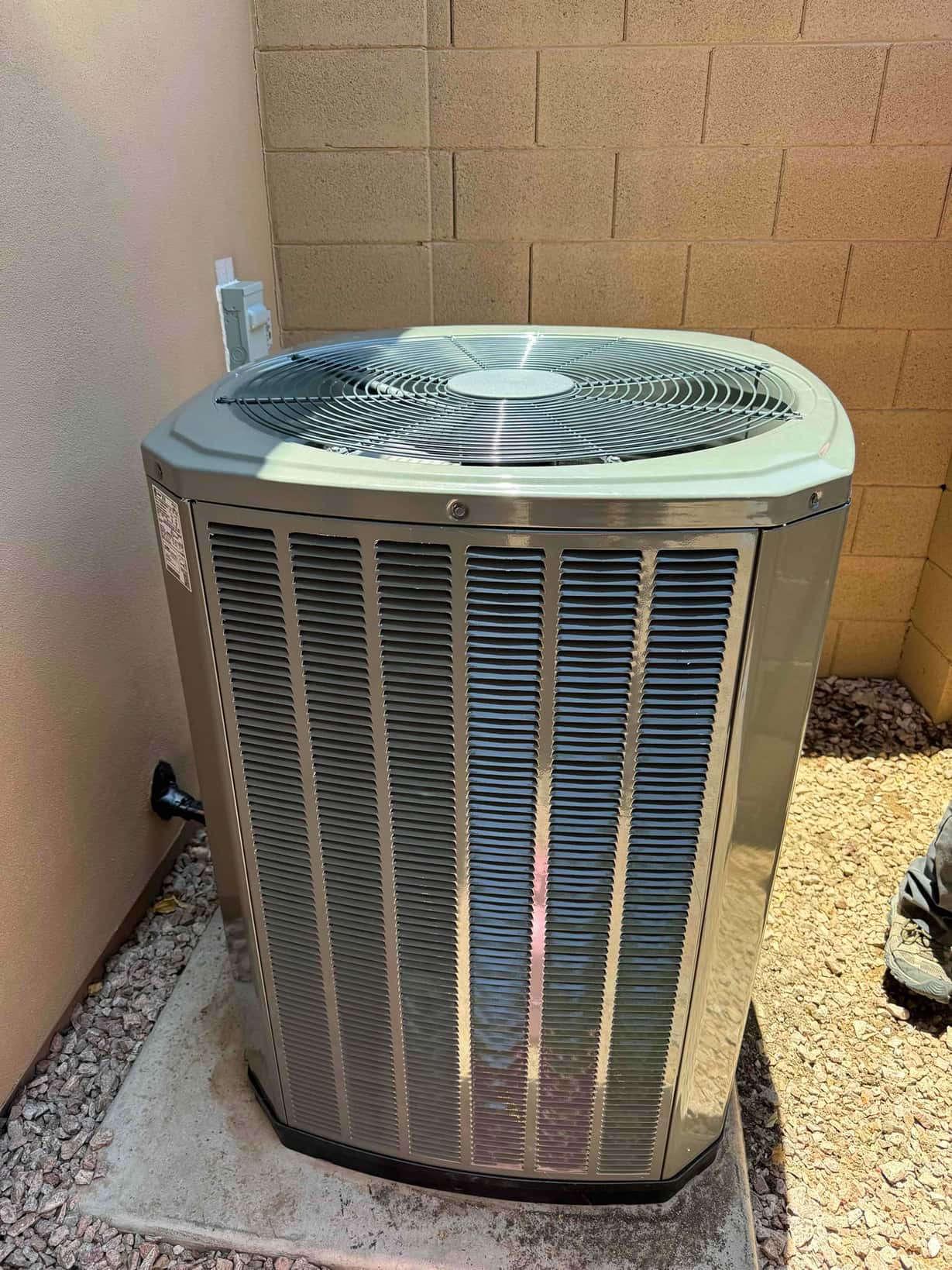 New outdoor condenser set on a level pad with nearby electrical disconnect, neatly installed against the exterior wall.