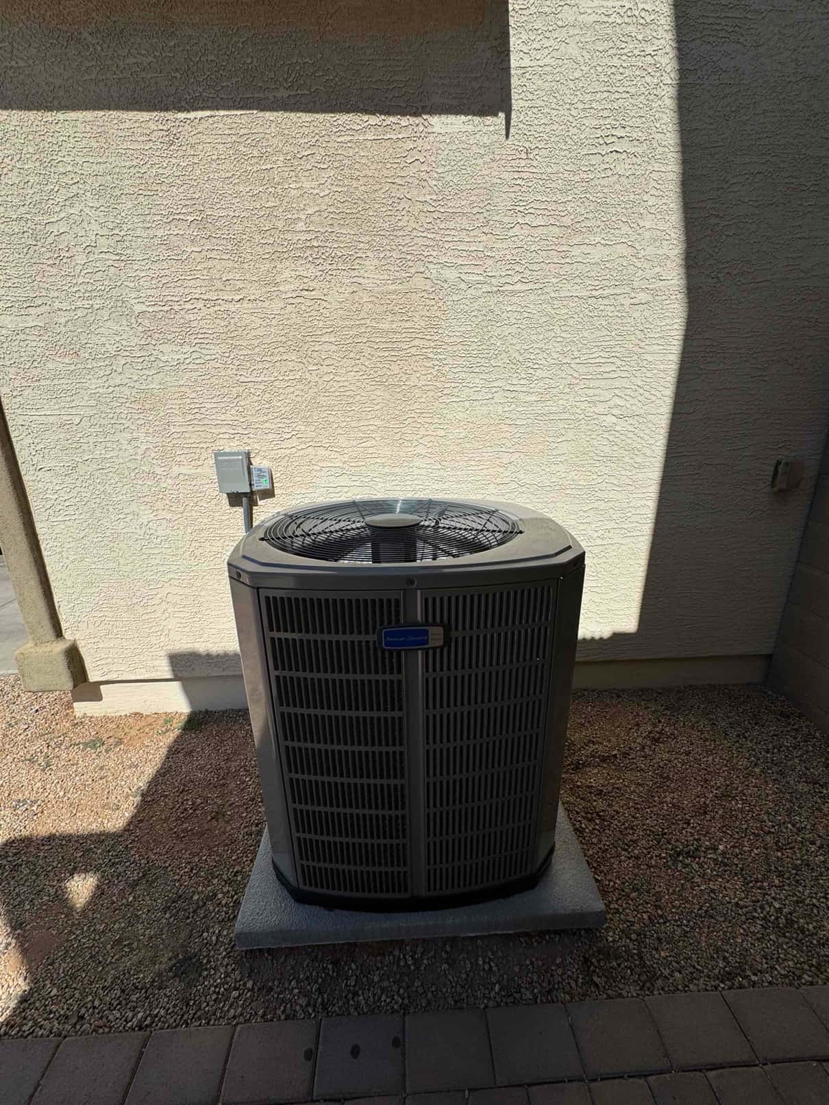 New outdoor condenser set on a level pad with nearby electrical disconnect mounted on the exterior wall.