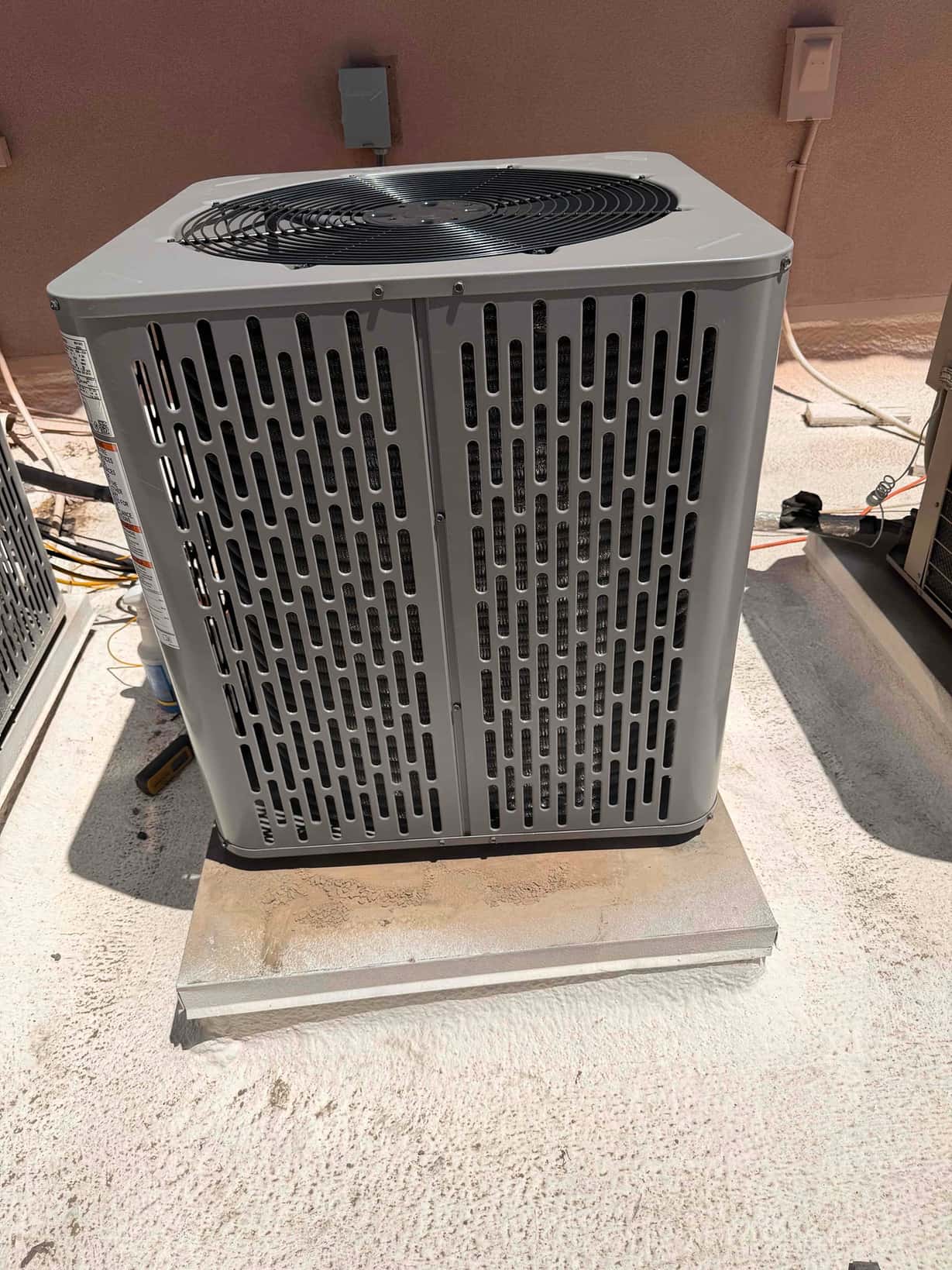 New outdoor condenser set on a level rooftop pad with electrical disconnect nearby and refrigerant line routing in progress.