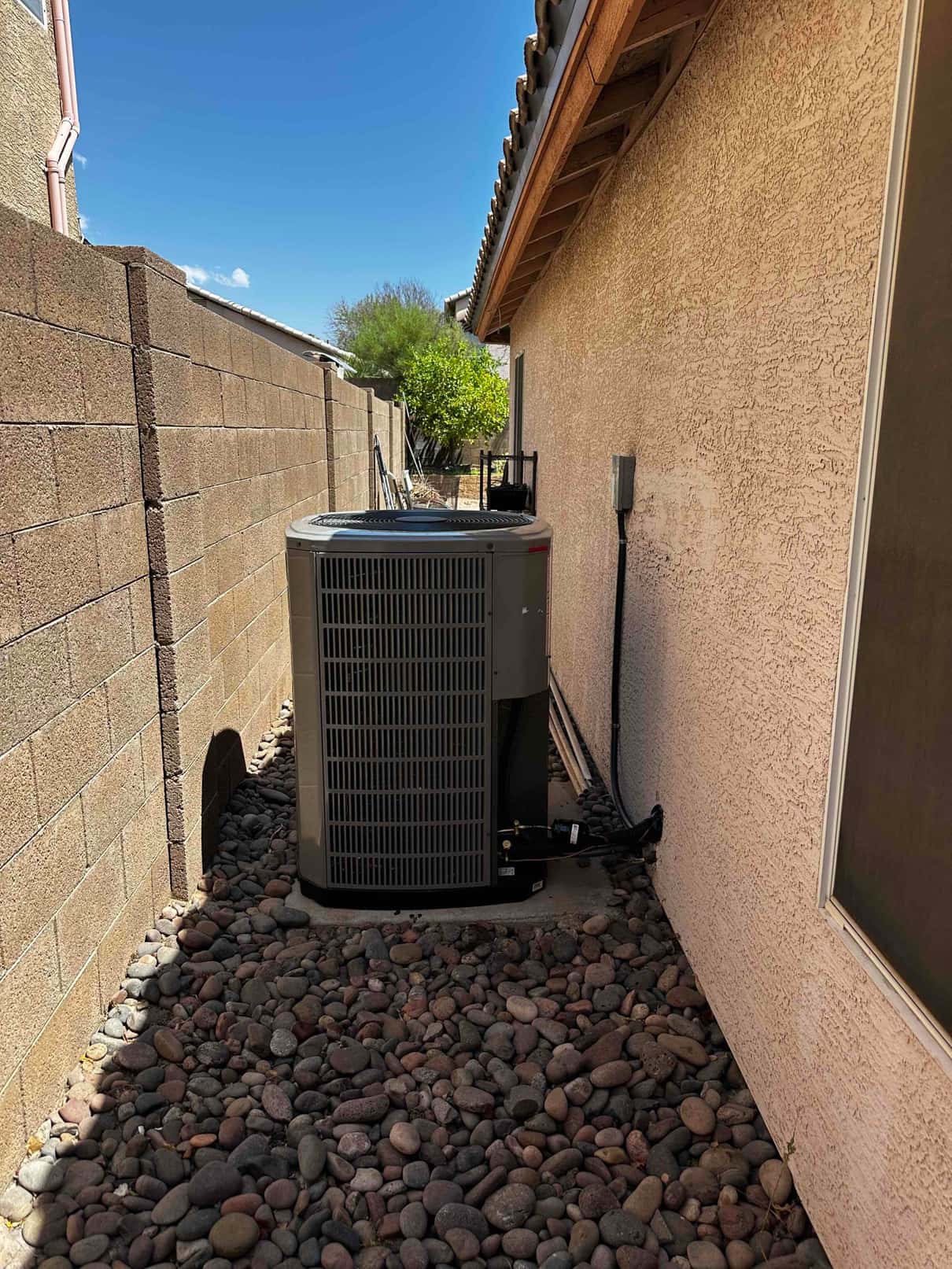 New outdoor heat pump condenser set on a level pad with insulated line set and wall-mounted disconnect.