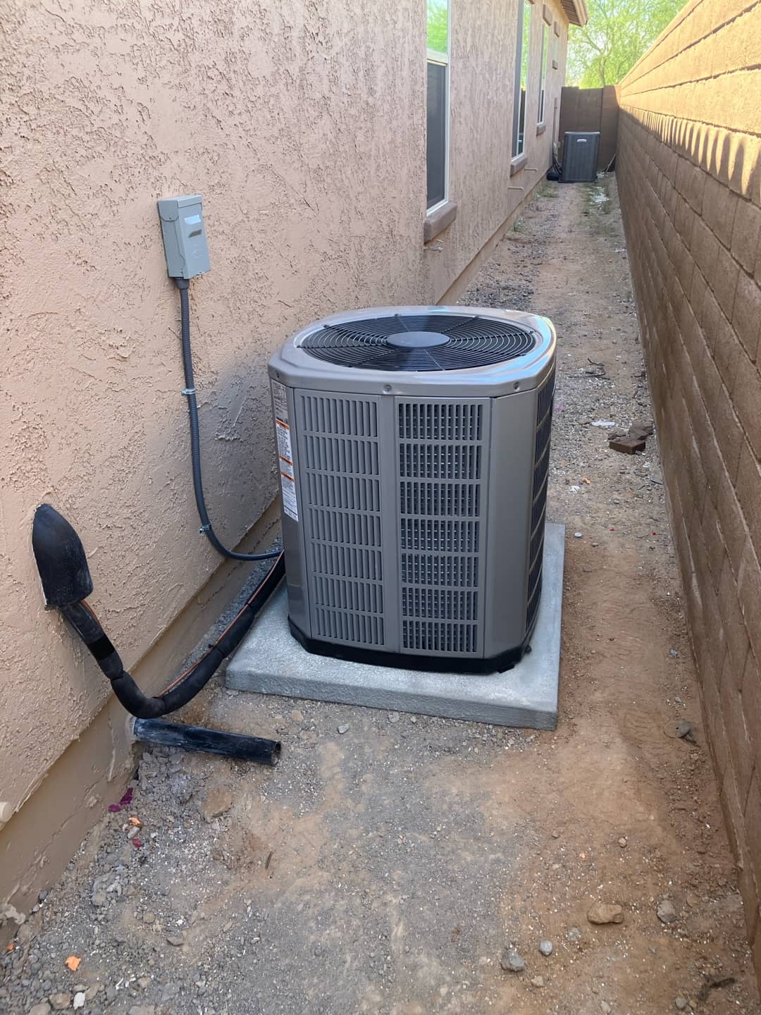 New outdoor heat pump condenser set on a level pad with weatherproof disconnect and insulated refrigerant line routing along the wall.