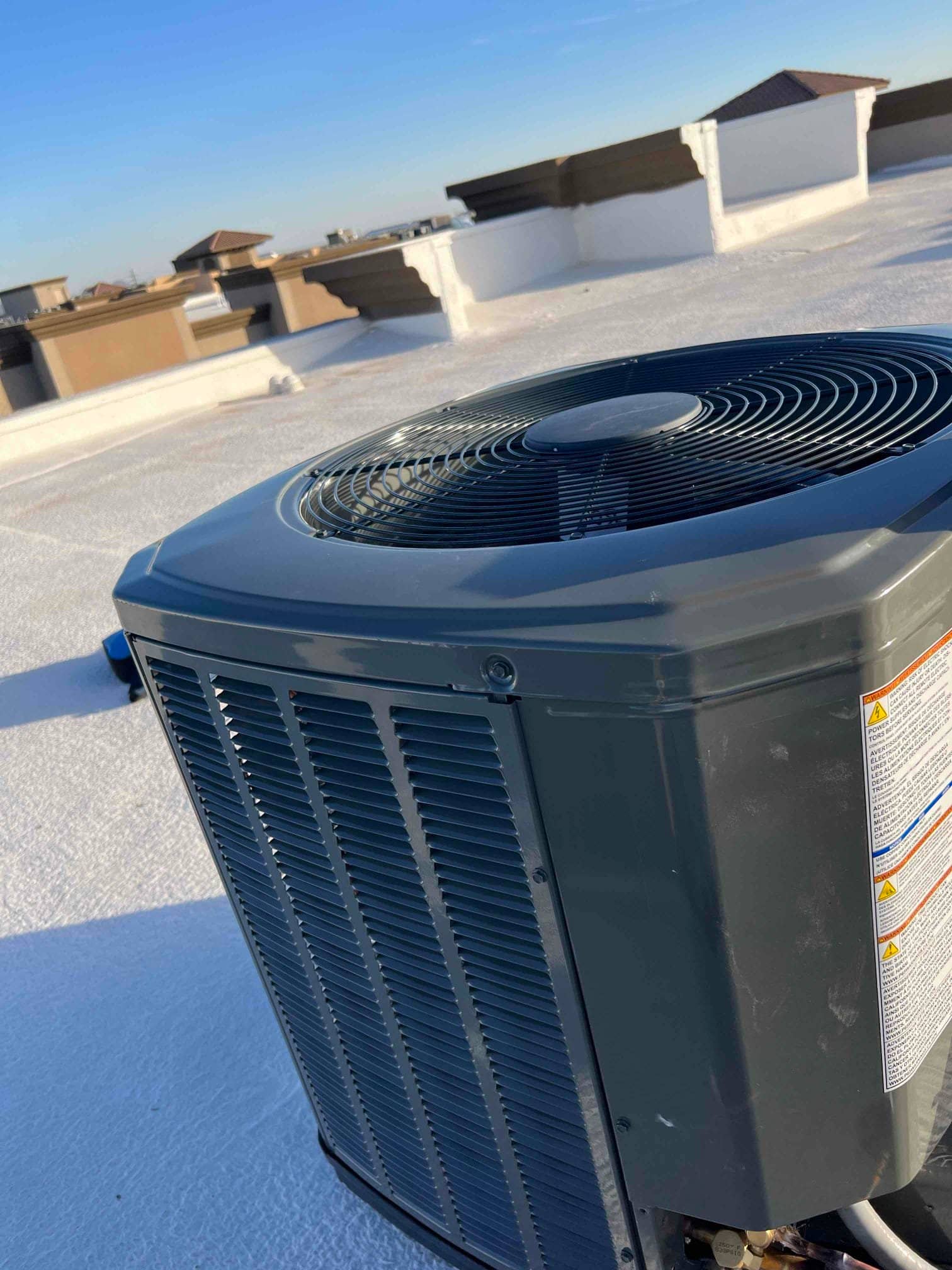 New rooftop condenser installed on a flat roof, with protective grille and service valves accessible on the side panel.
