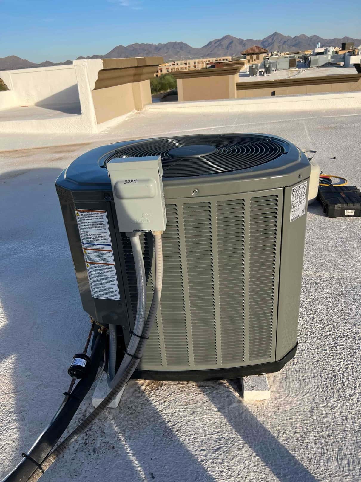 New rooftop condenser set on risers with insulated refrigerant lines and weatherproof disconnect installed beside the unit.