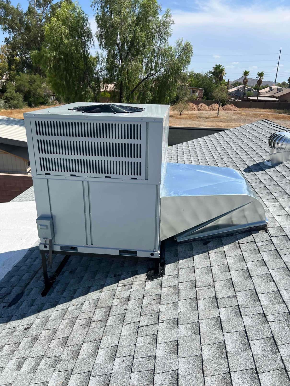 New rooftop package heat pump set on a metal stand with sealed supply duct transition and exterior disconnect box.