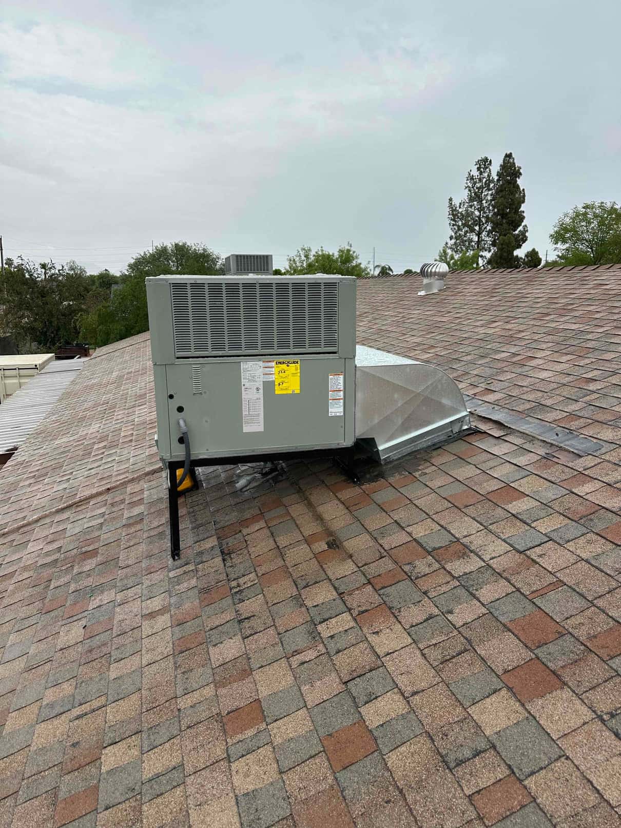 New rooftop package HVAC unit set on a stand with duct connection and electrical whip routed on the shingle roof.