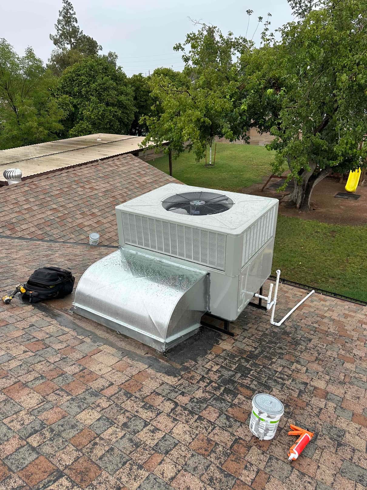 New rooftop package unit set with curb adapter, sealed duct connection, and condensate piping visible alongside roofing tools.