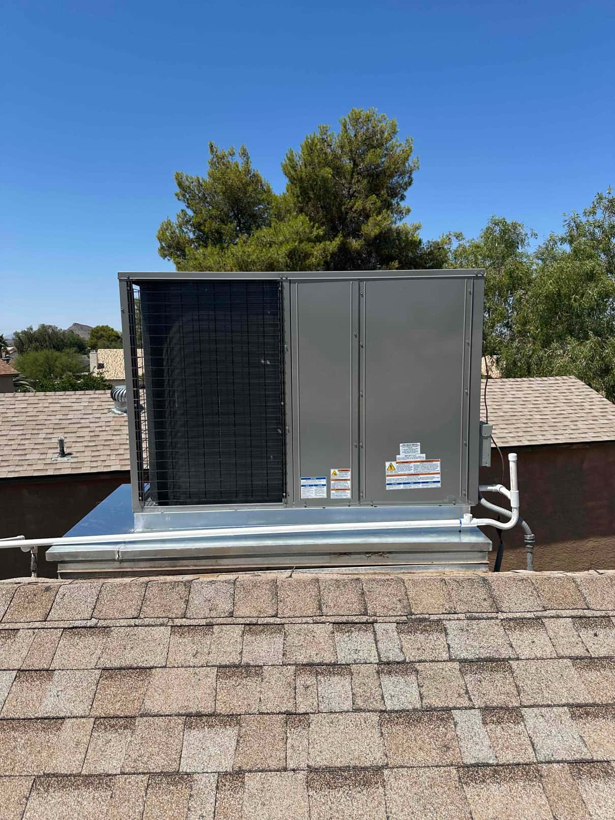 New rooftop packaged heat pump set on a curb with sealed ducts and condensate piping, photographed after installation under clear skies.