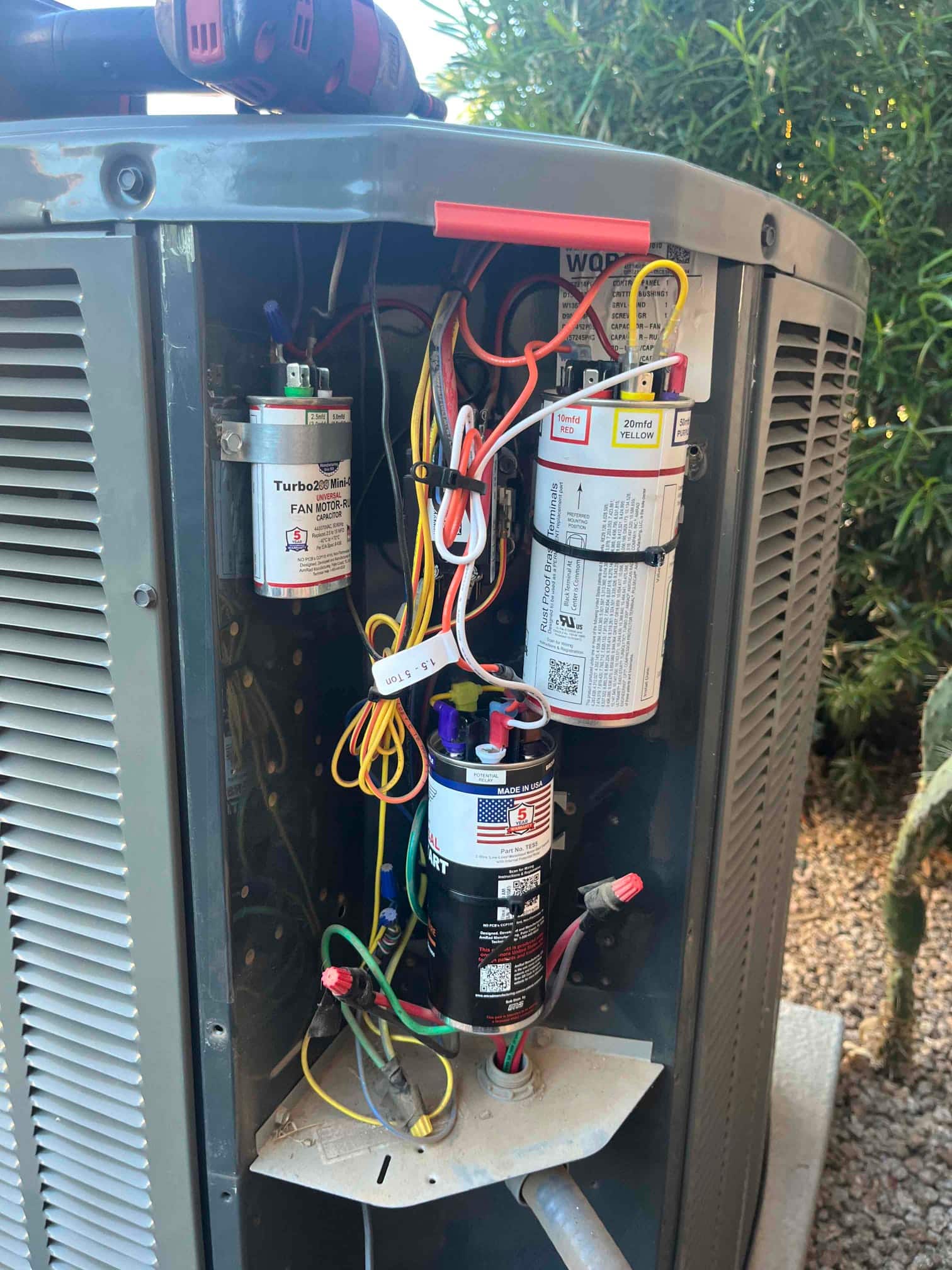 Outdoor condenser control compartment open, showing new dual-run capacitor, start assist module, and neatly routed wiring connections.