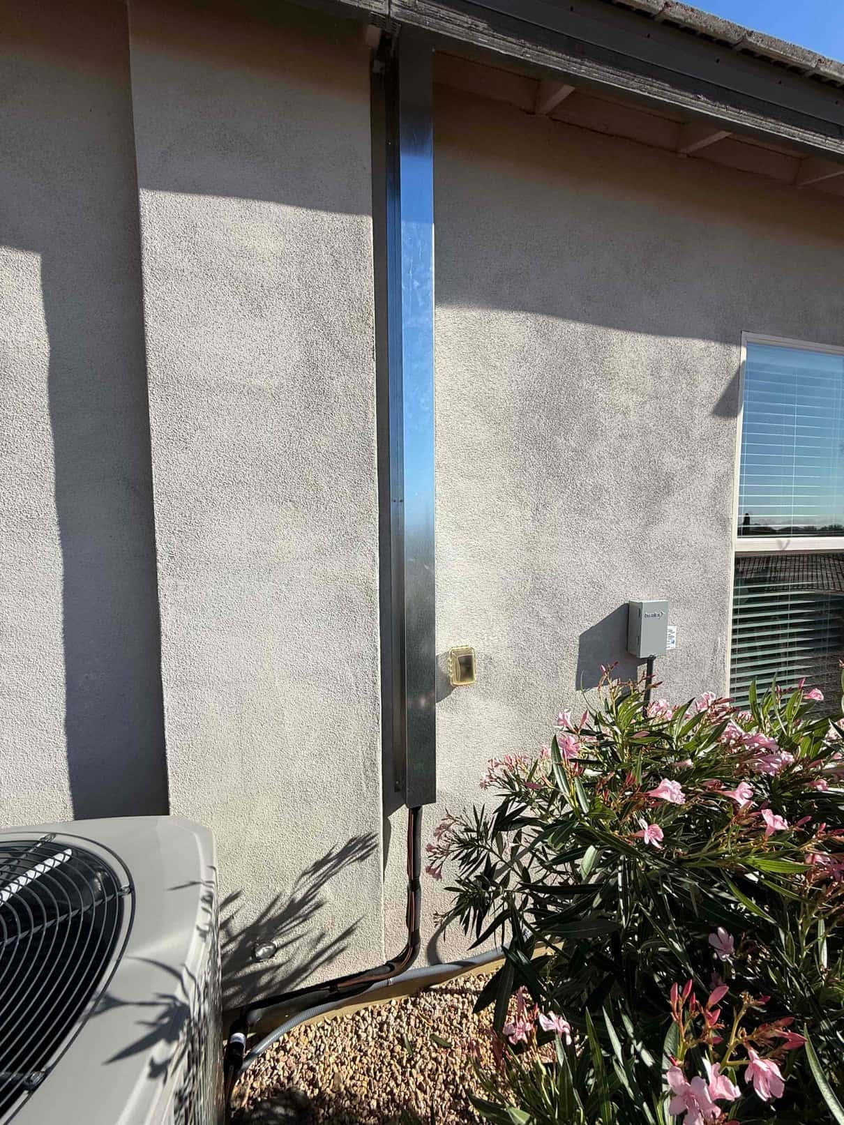 Outdoor condenser with insulated refrigerant lines routed in a vertical metal line hide, alongside disconnect and sealed wall penetration.