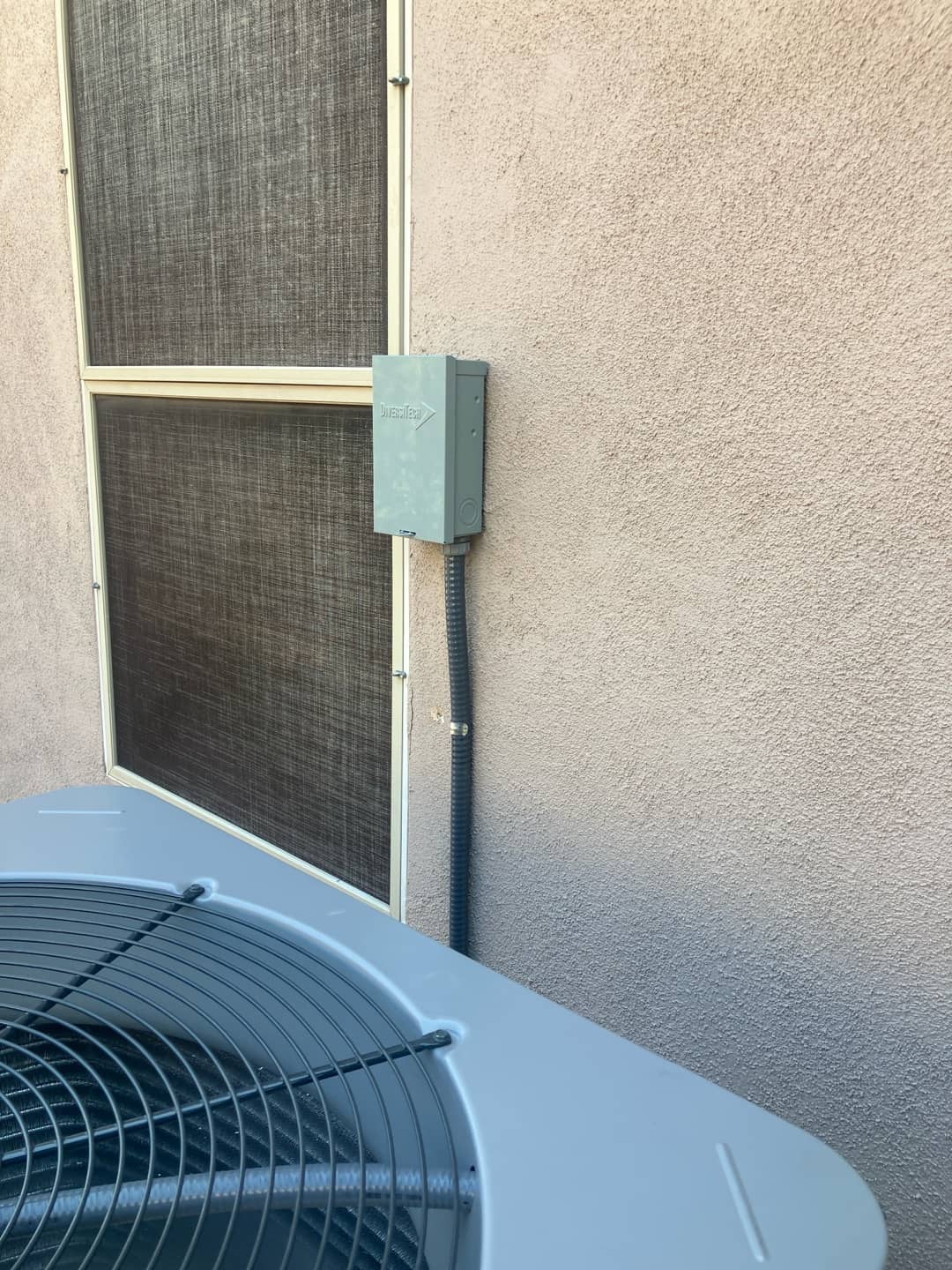 Outdoor condenser next to a mounted weatherproof disconnect with flexible conduit neatly routed along the exterior wall.