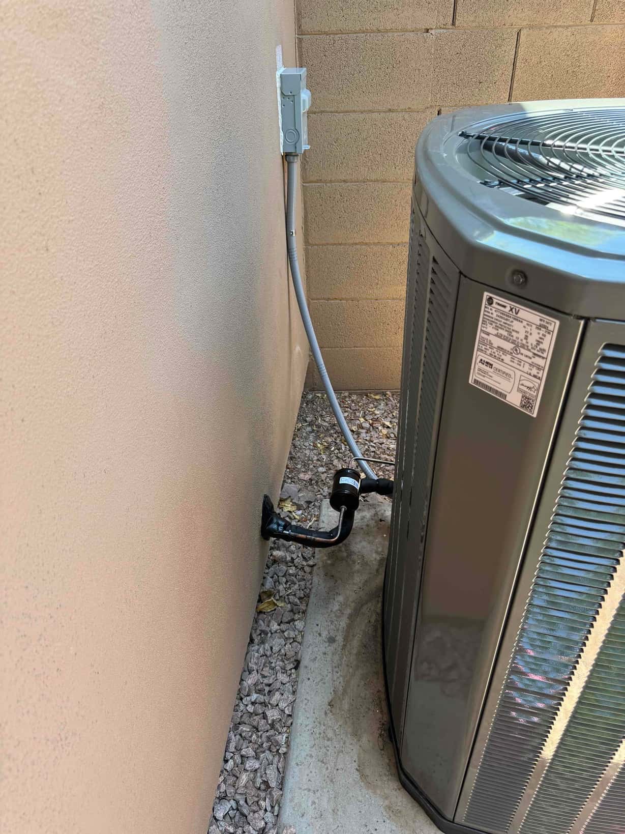 Outdoor condenser set on a level pad with insulated line set, suction filter-drier, and weatherproof electrical disconnect installed.