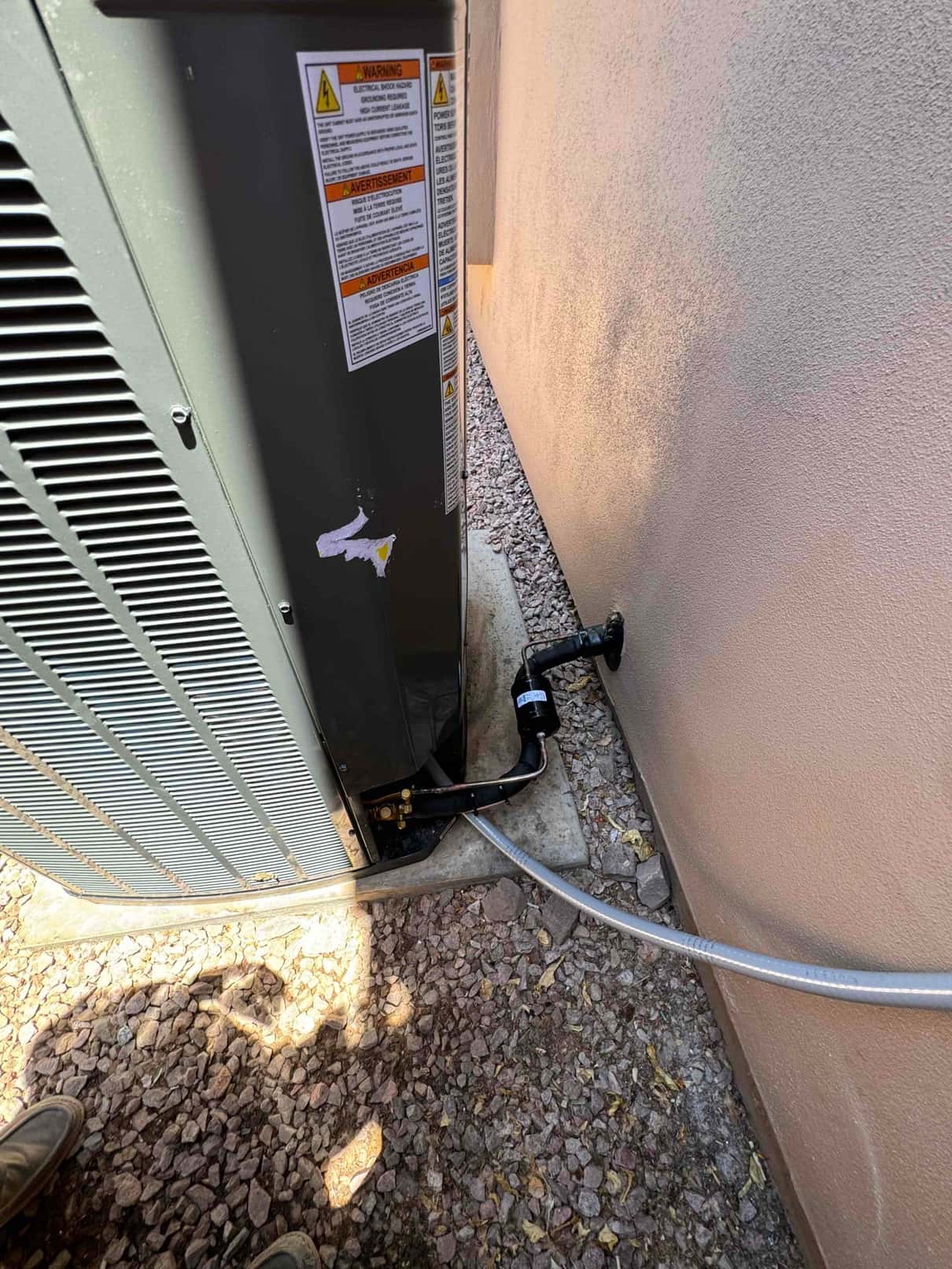 Outdoor condenser set on a level pad with insulated refrigerant lines, filter drier, and flexible electrical conduit neatly routed.