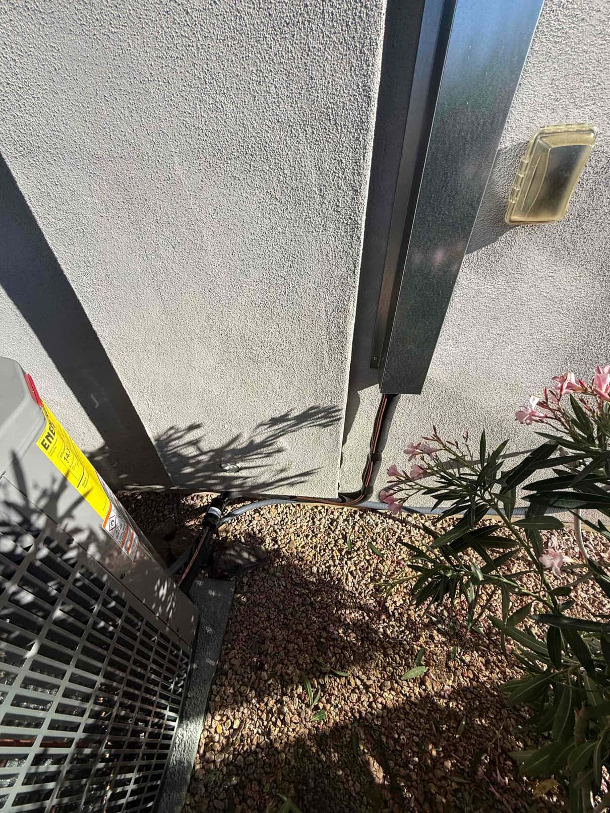 Outdoor condenser set on a pad with line set and electrical conduit secured along the exterior wall above landscape gravel.