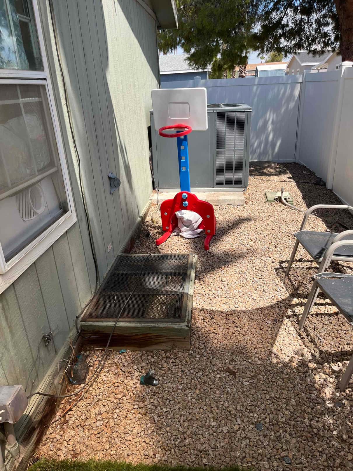 Outdoor condenser unit beside a house with adjacent disconnect box and gravel work area visible.
