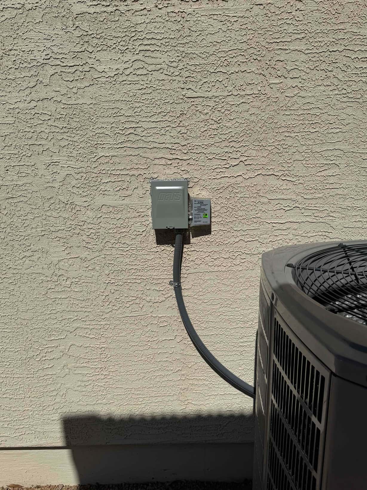 Outdoor disconnect box with flexible conduit neatly routed to a newly installed heat pump condenser on a level pad.