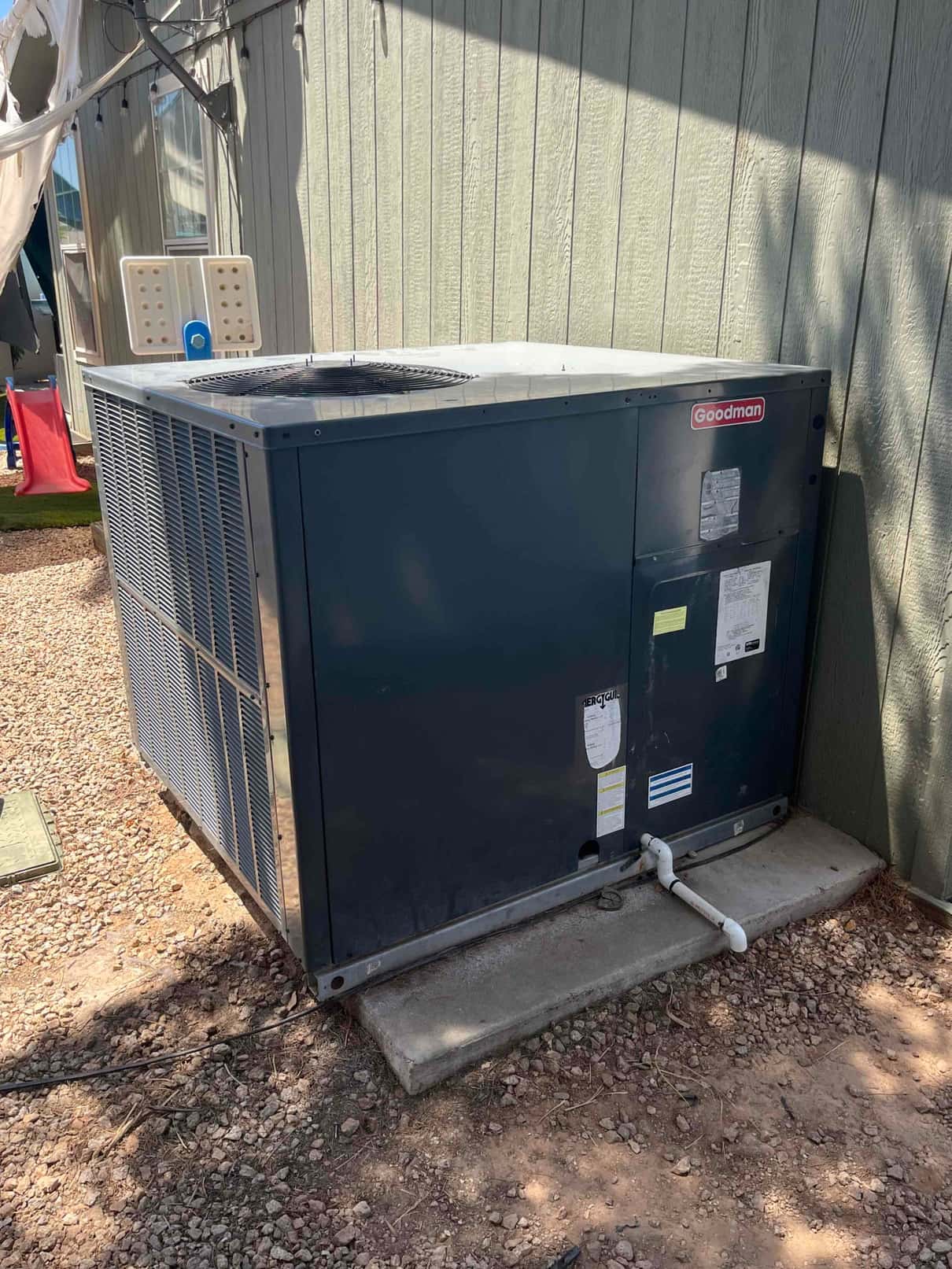 Outdoor HVAC condenser unit on a concrete pad, showing weathered cabinet, service panels, and condensate drain line.