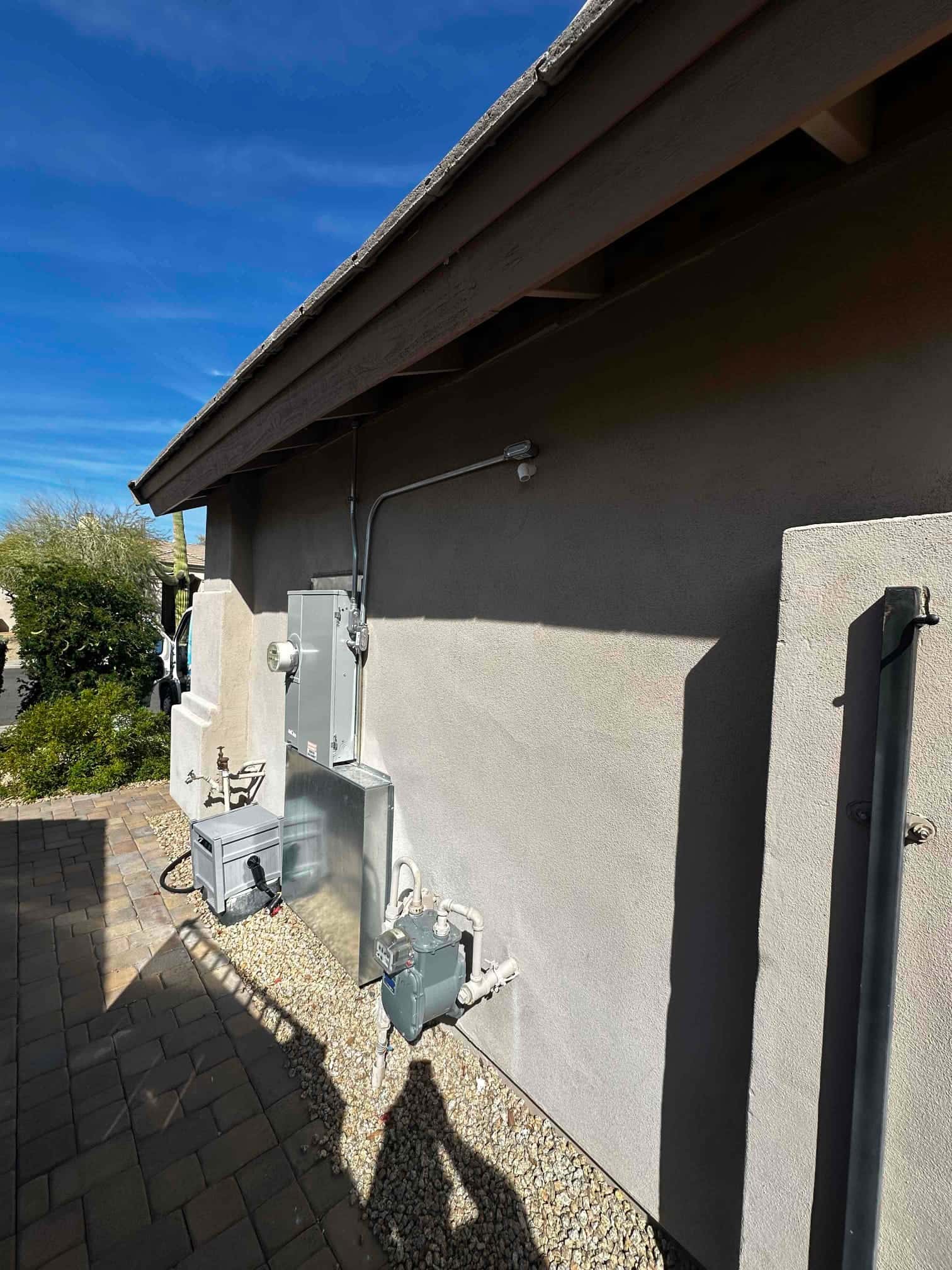 Outdoor installation area showing new mini-split condenser on pad with insulated line set, electrical disconnect, and sealed wall penetration.