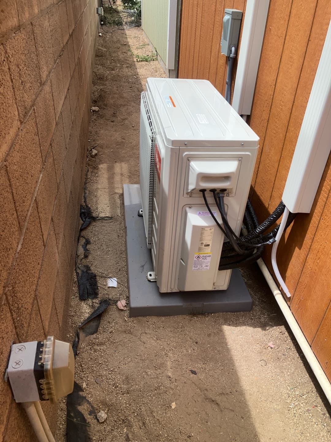 Outdoor mini-split condenser set on a level pad with line set cover and weatherproof electrical disconnect mounted on the wall.