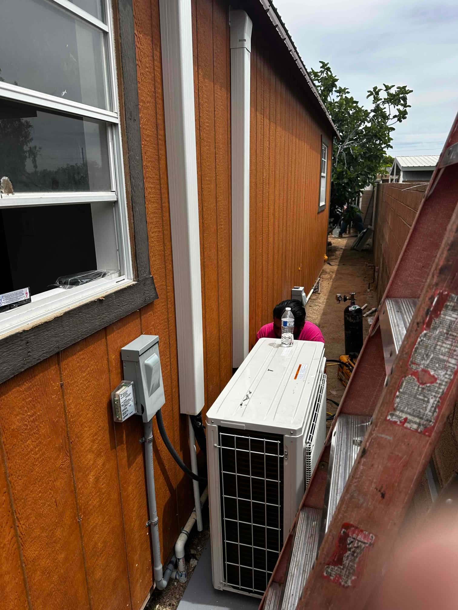 Outdoor mini-split condenser set on a level pad with line hide, electrical disconnect, and condensate drain installed along the wall.