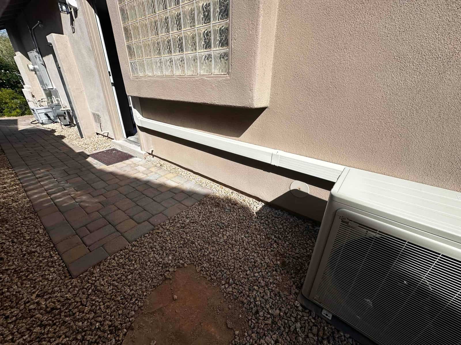 Outdoor mini-split condenser set on a pad with line-set cover secured along the exterior wall to the indoor entry.