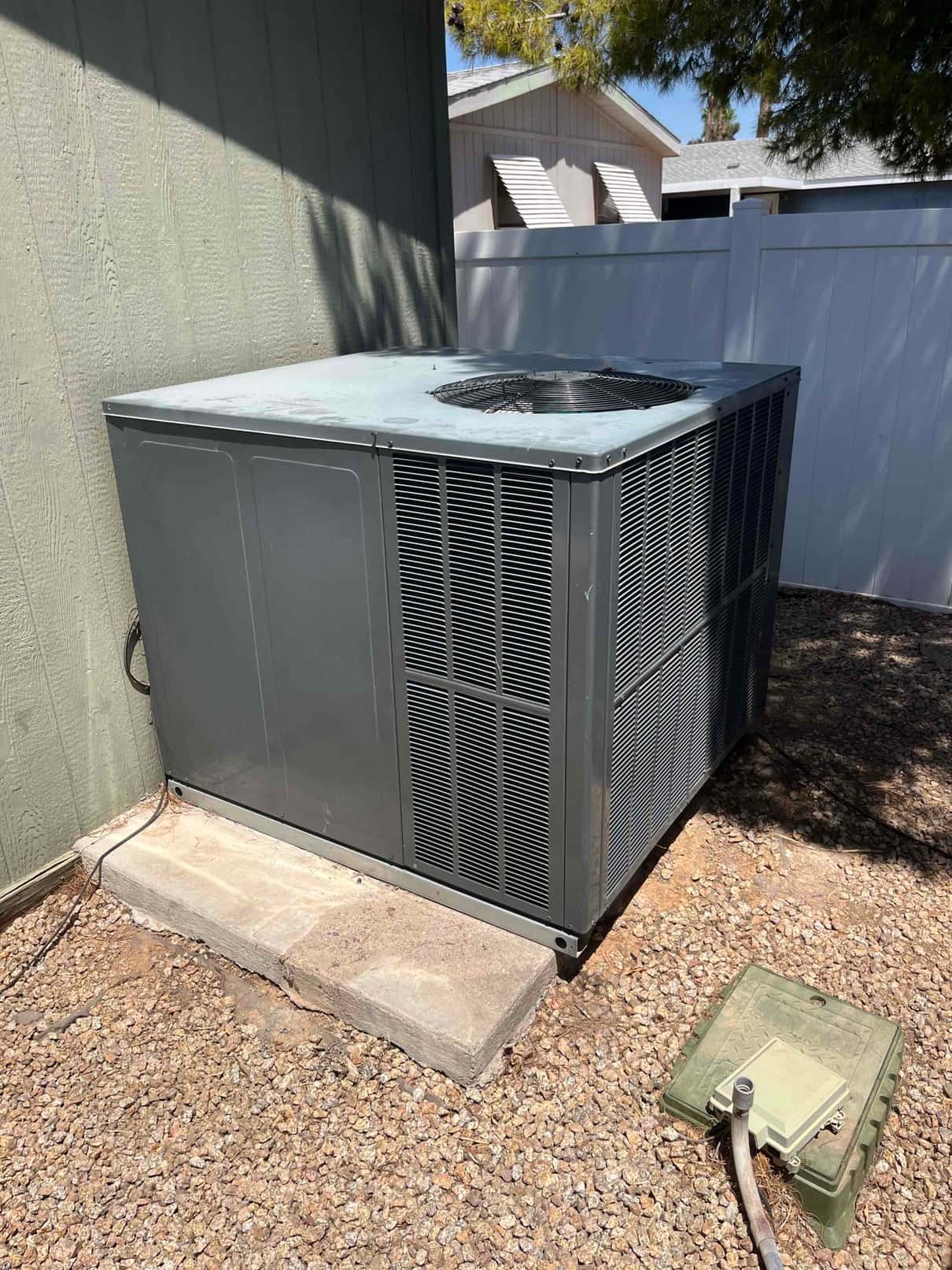 Package HVAC condenser unit outdoors on a pad, with service disconnect box open beside the gravel area.