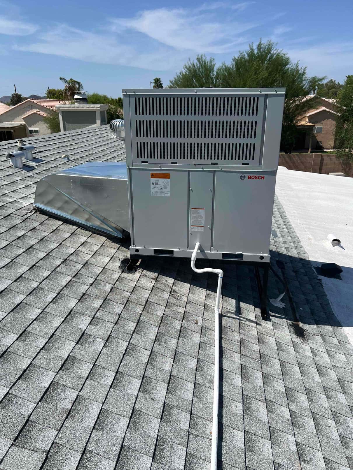 Packaged rooftop heat pump installed on stands with new duct transition and condensate drain routed across the shingle roof.