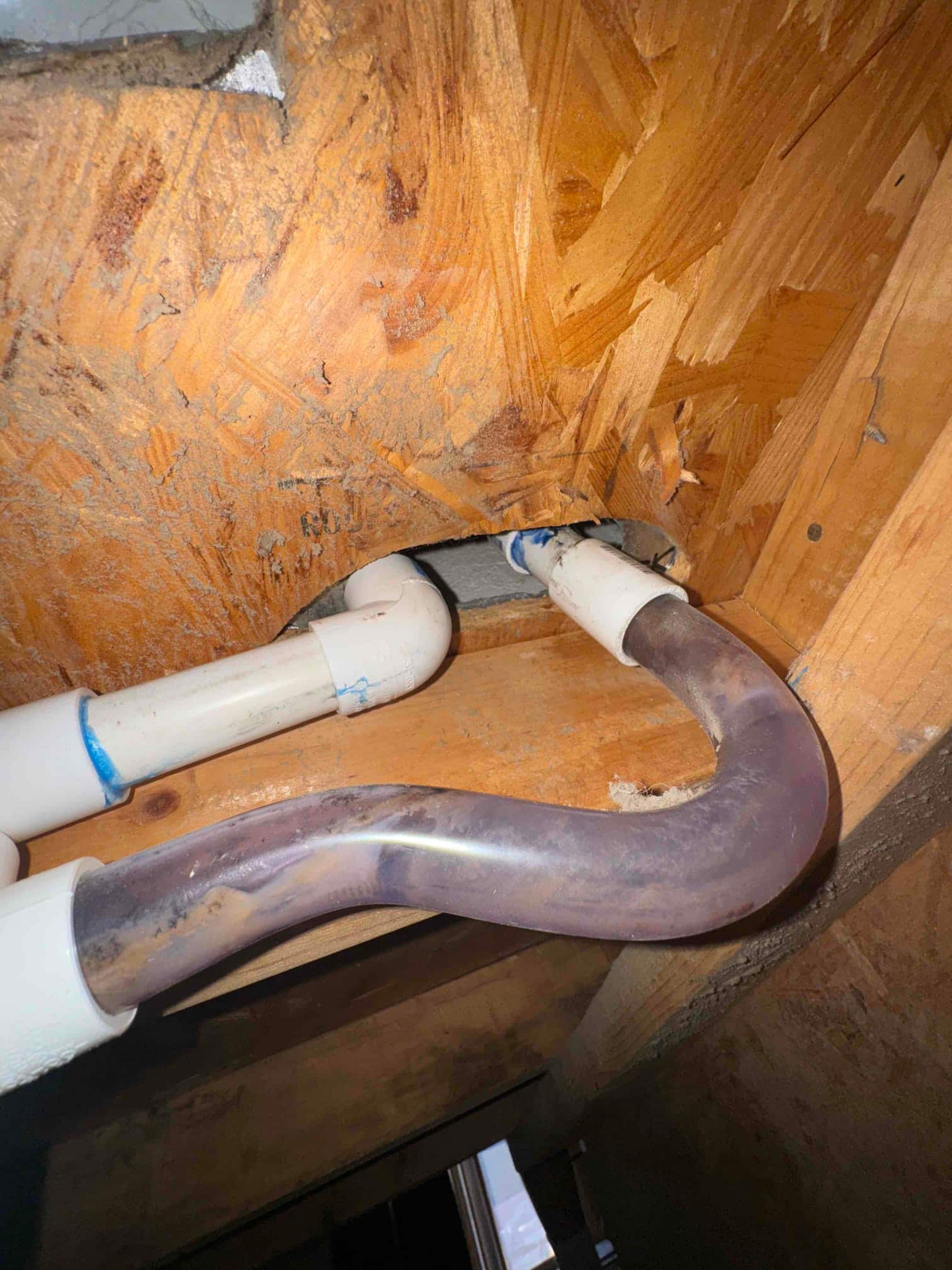 PVC condensate drain piping with a clear trap section routed through a joist opening inside the air handler area.