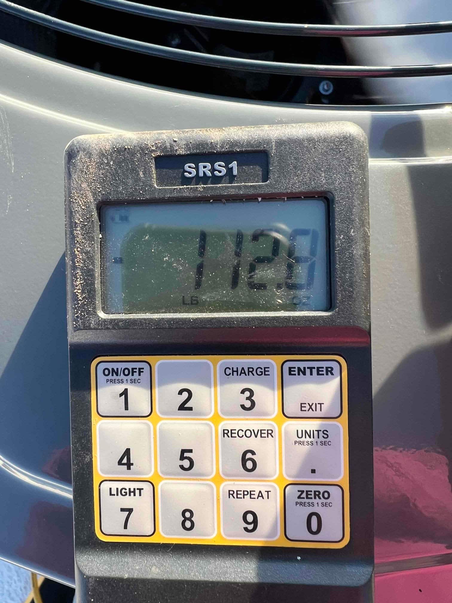 Refrigerant charging scale on top of an outdoor unit displays 11.28 pounds during system charging process.