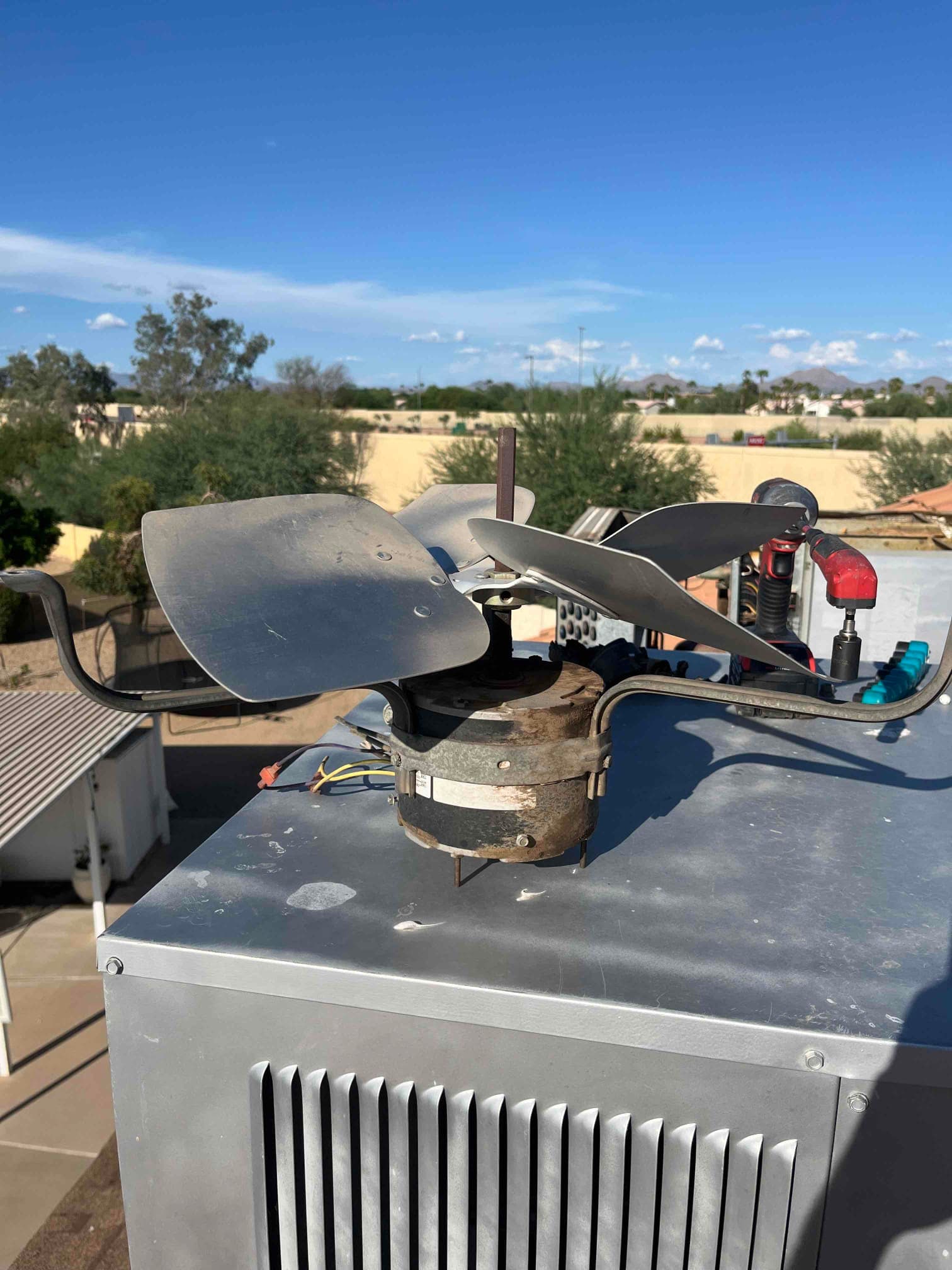Removed condenser fan motor with damaged, bent fan blades sitting on top of the outdoor unit housing.
