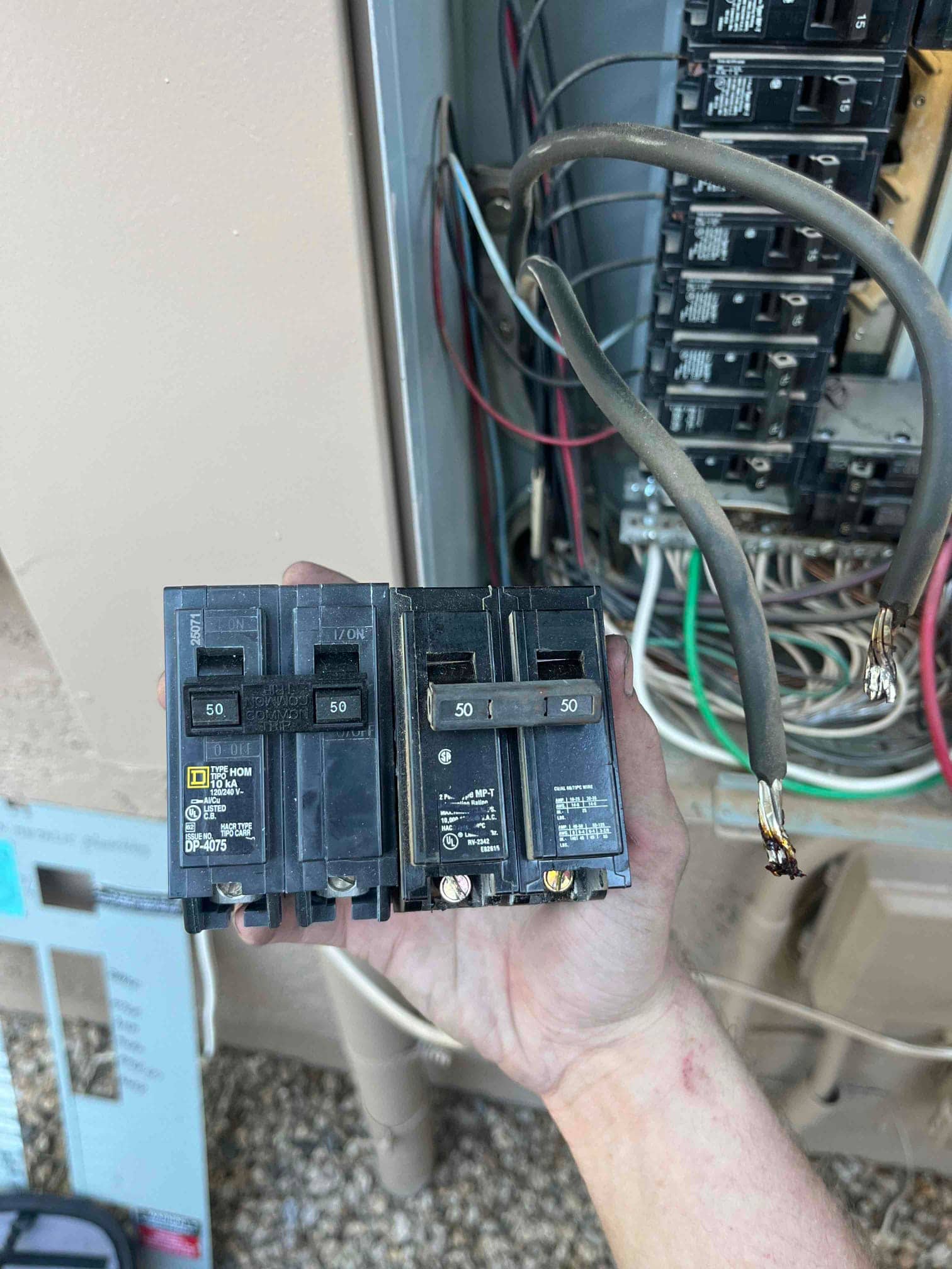 Removed double-pole circuit breakers rated 50A held near an open electrical panel with detached, stripped conductors visible.