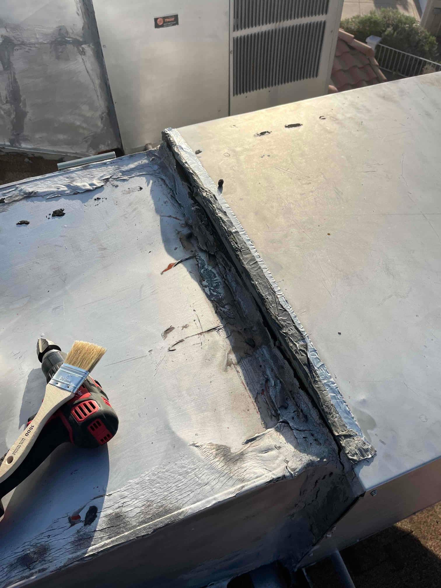 Rooftop HVAC sheet metal housing with sealed seam and applied mastic, next to a brush and drill driver.