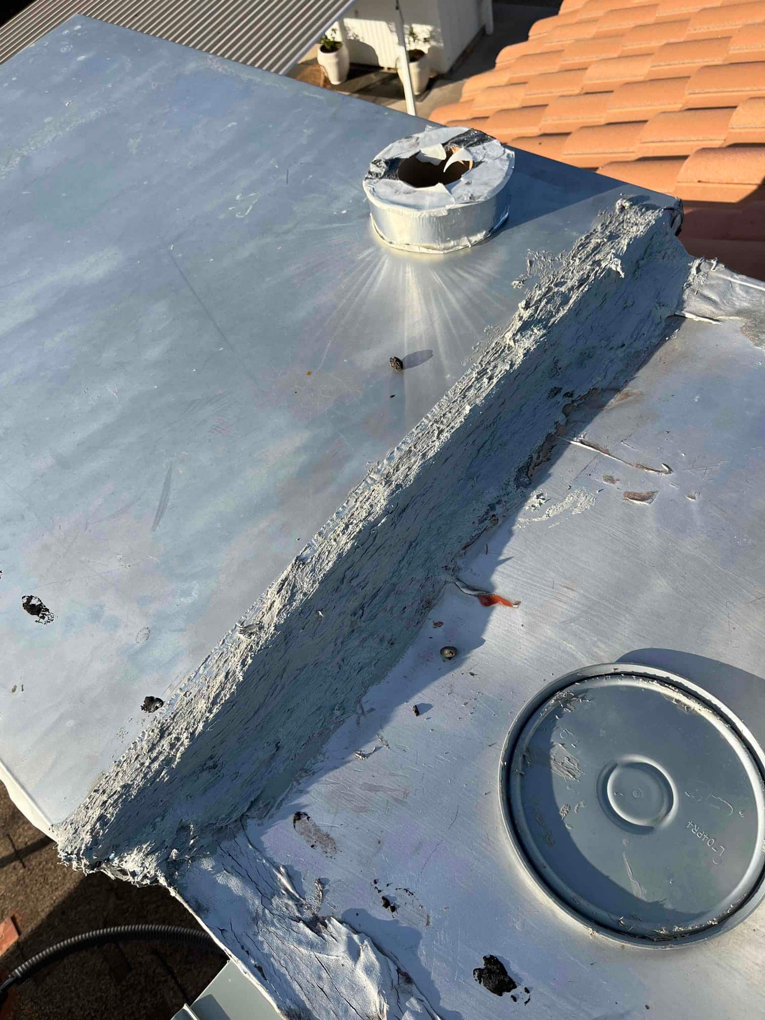 Rooftop HVAC unit top panel with heavy sealant along a seam and circular duct openings visible.
