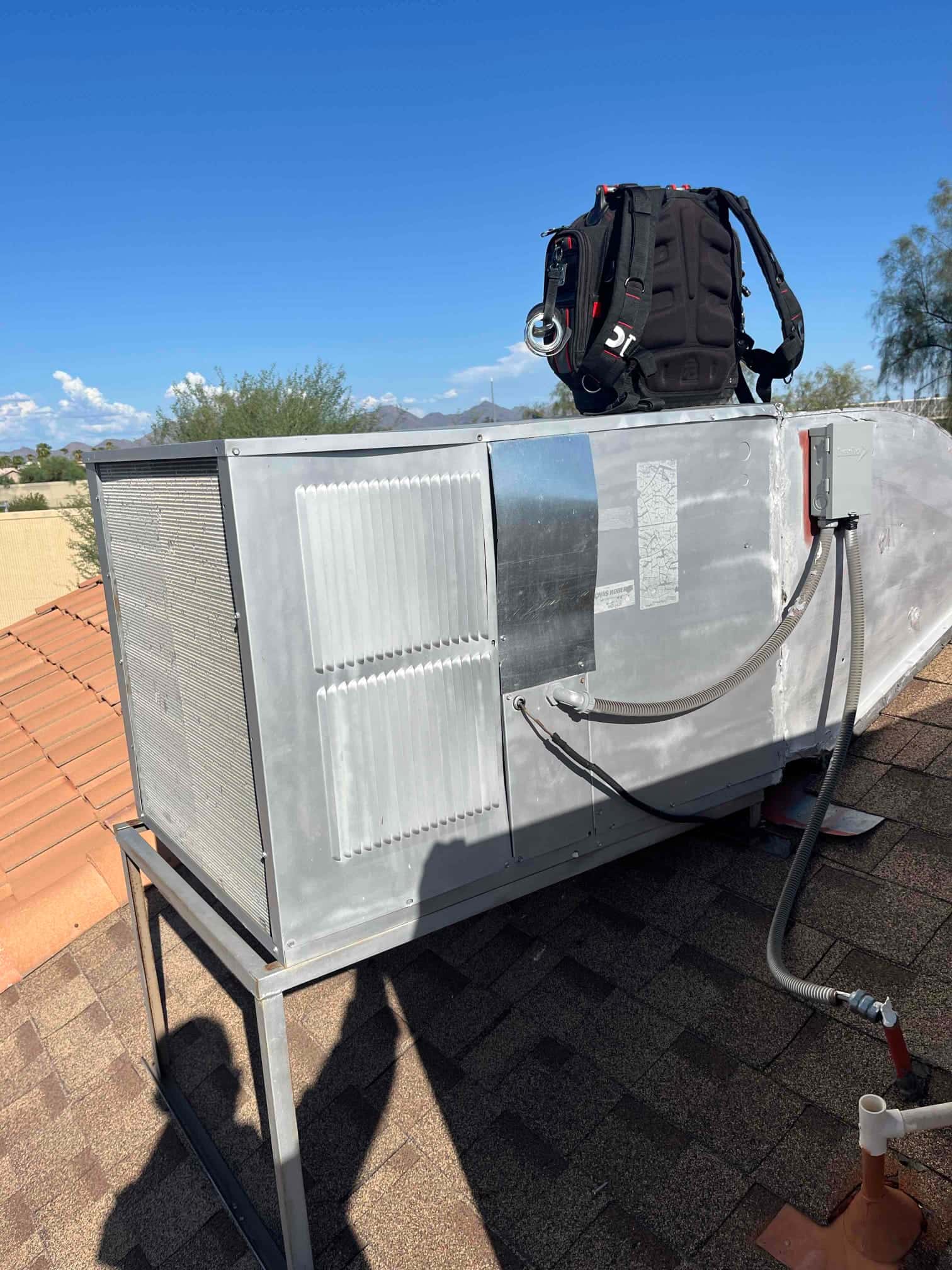 Rooftop package HVAC unit on a stand with exterior panels and electrical disconnect box visible beside the cabinet.
